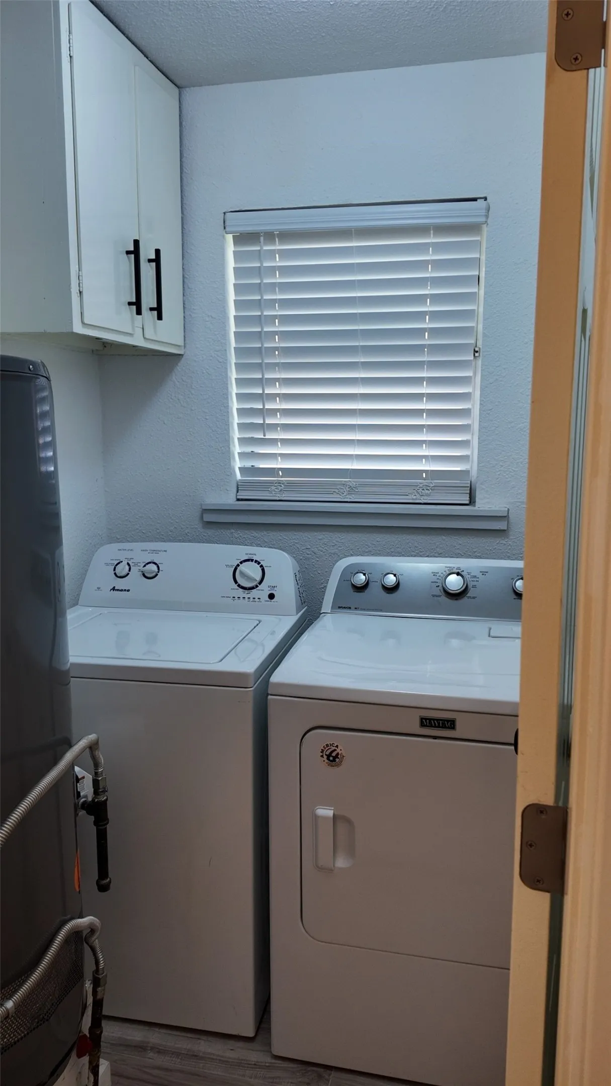 Laundry area with white cabinetry, matte black hardware, horizontal blinds, and wood-finish flooring