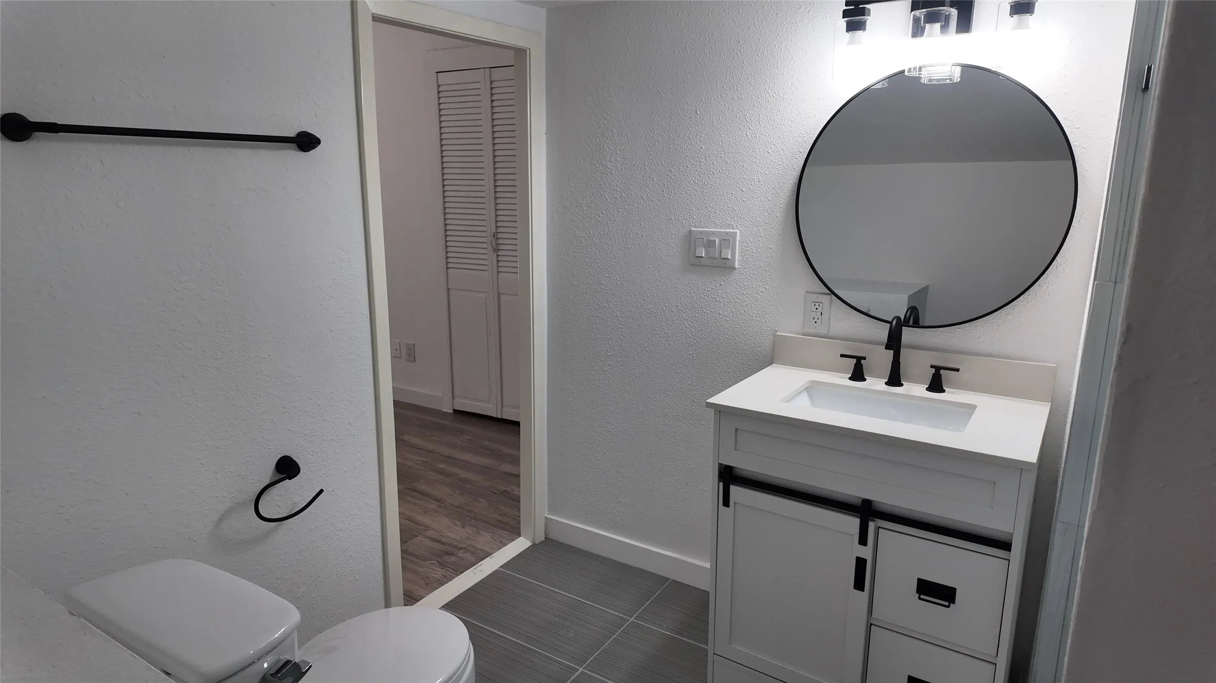 Modern vanity with a white countertop and integrated sink, matte black faucet, and a round mirror