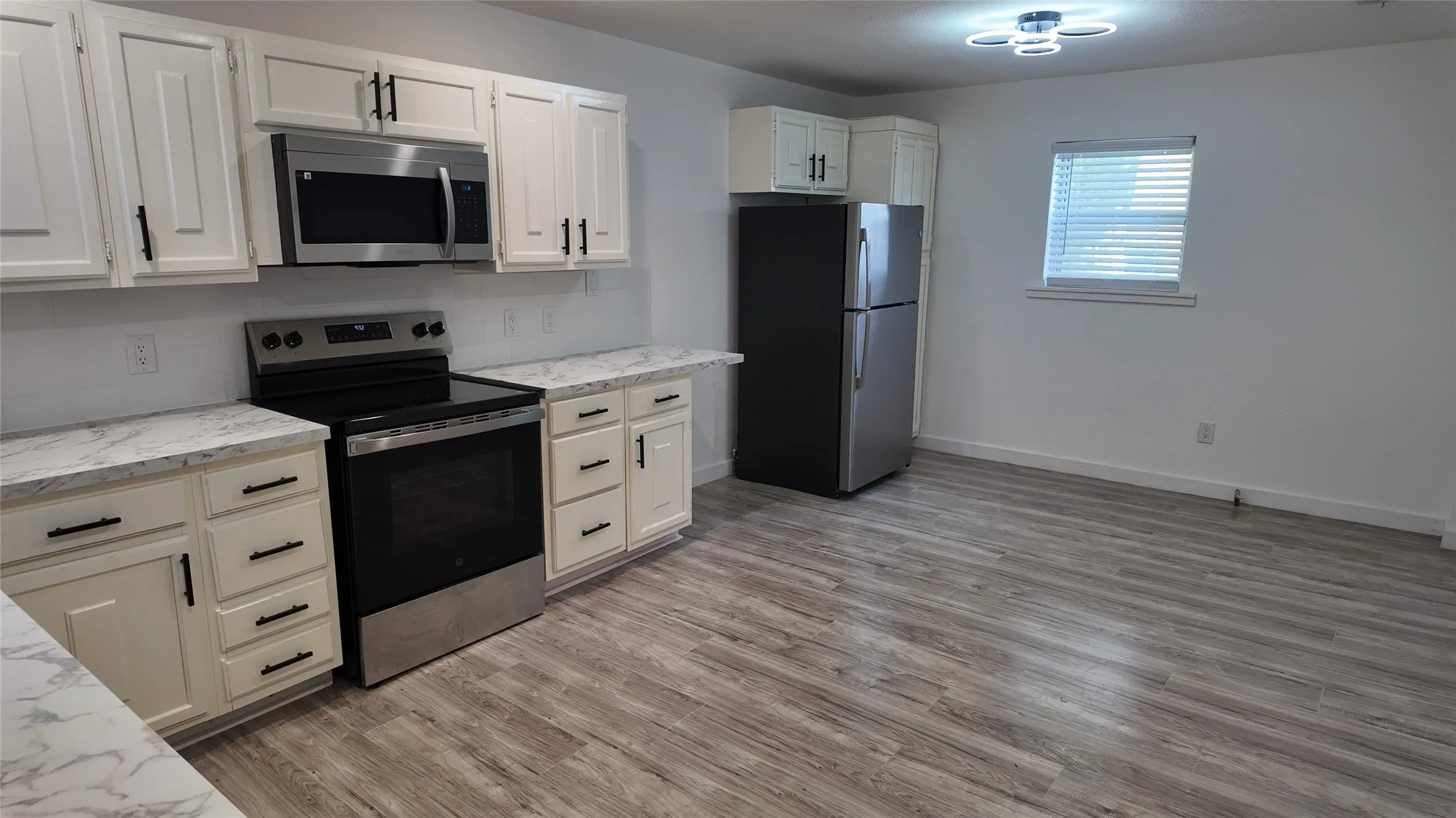 Kitchen featuring white cabinetry, stainless steel appliances, wood-finish flooring, and light-toned countertops