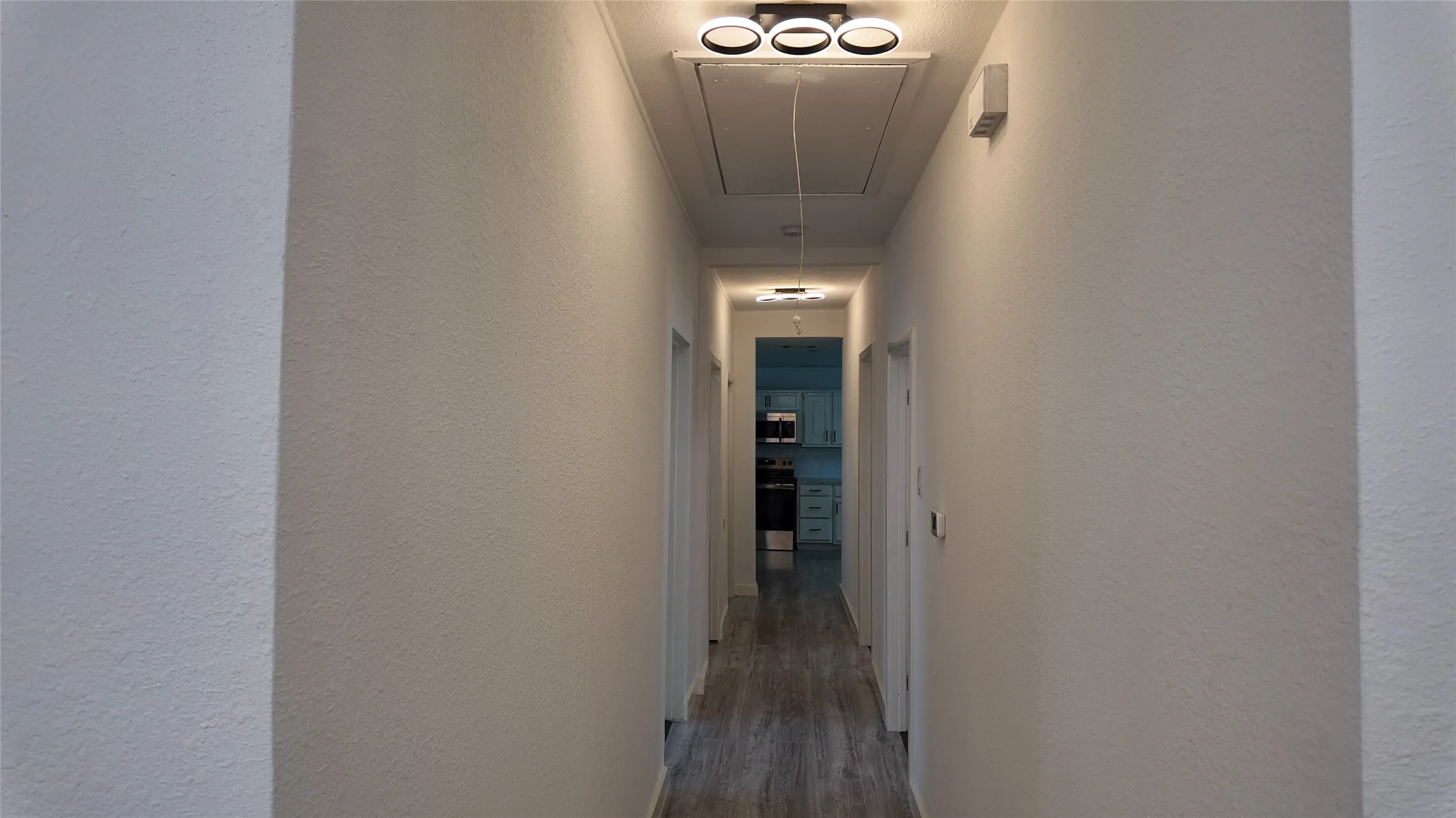 Hallway with wood-finish flooring, white painted walls, and modern flush-mount lighting fixtures