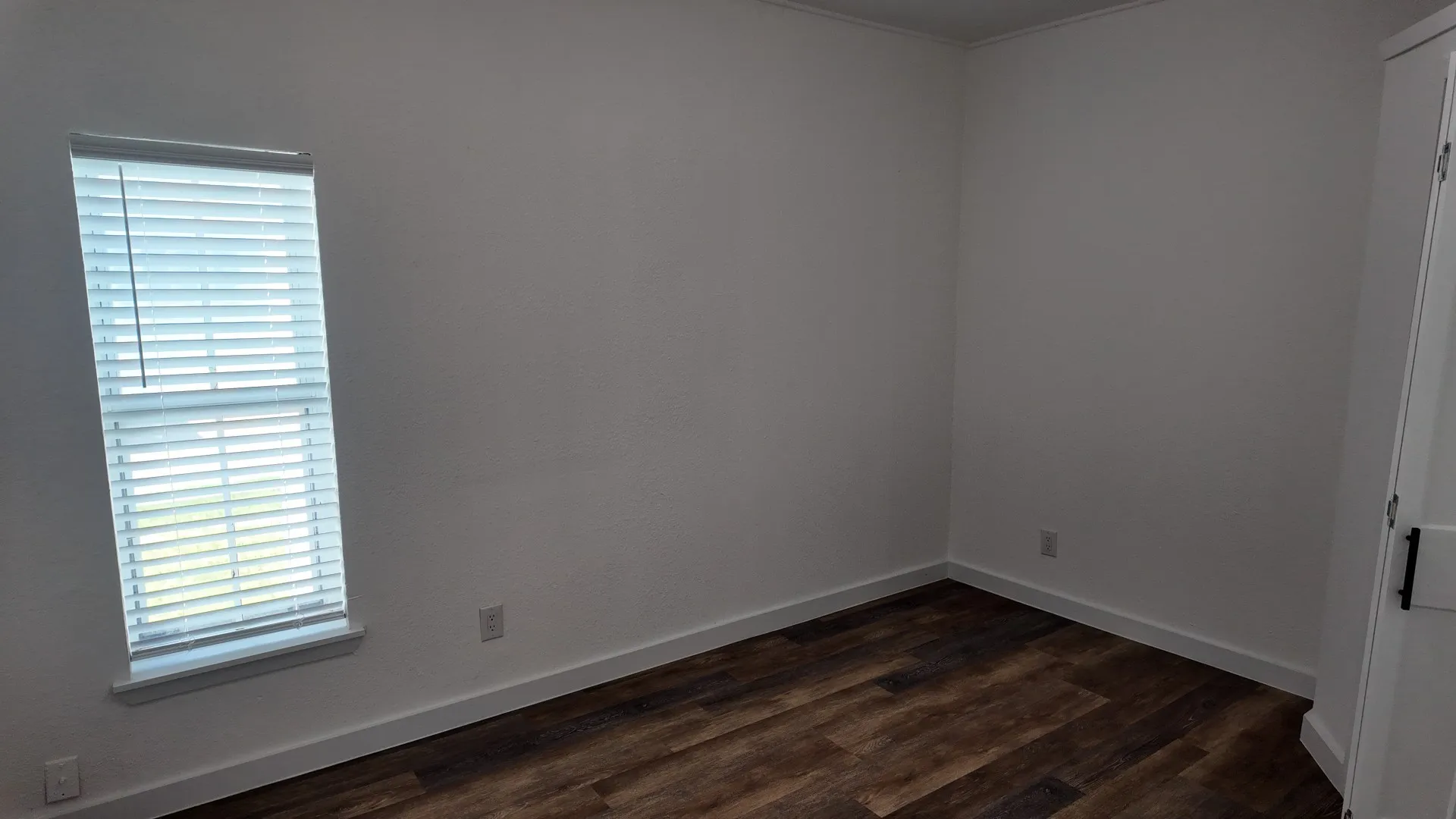 Wood-finish flooring, white walls, and a window with blinds