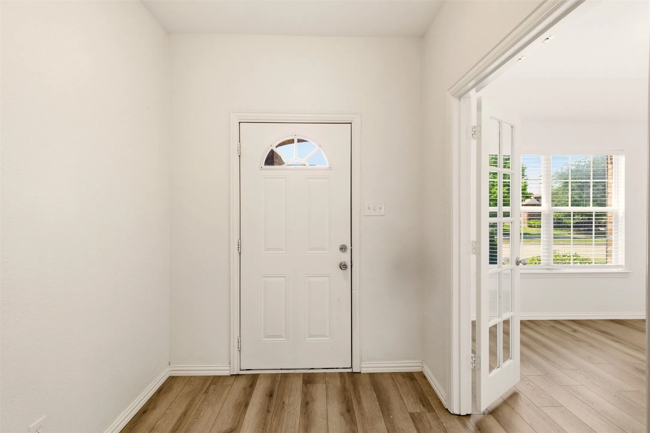 Entryway featuring a white door with an arched glass insert, wood-finish flooring, and white walls