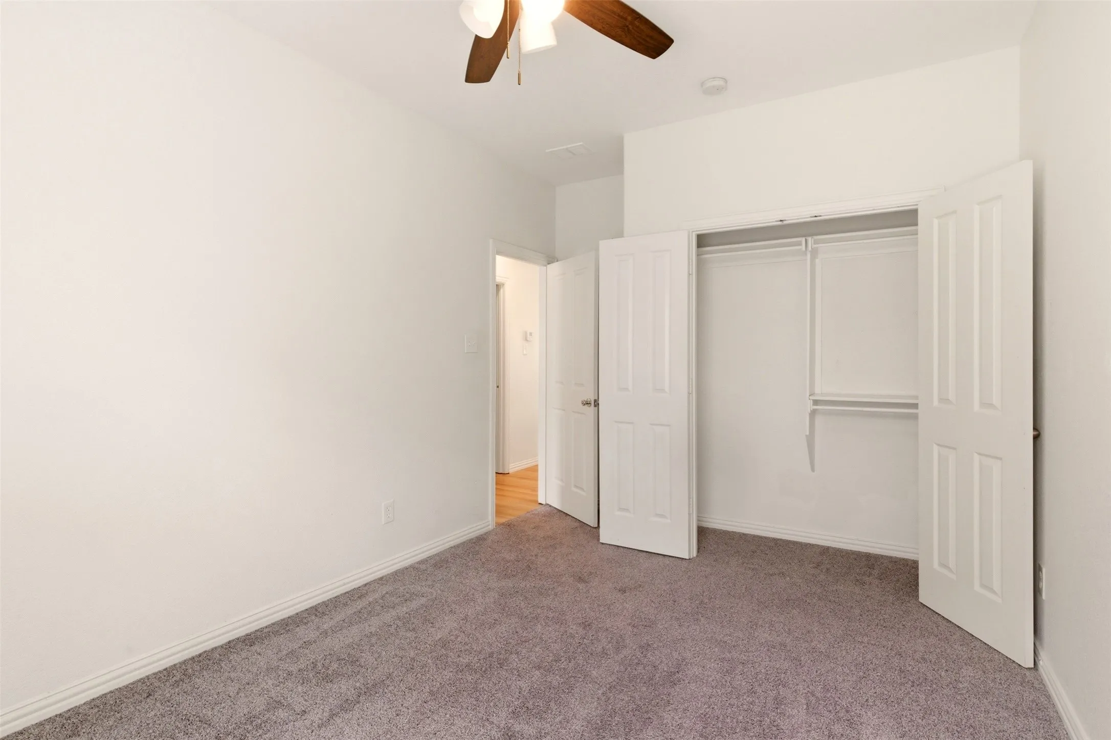 Gray carpeting, ceiling fan with integrated lighting, double-door closet with shelving and hanging rods, and white trim