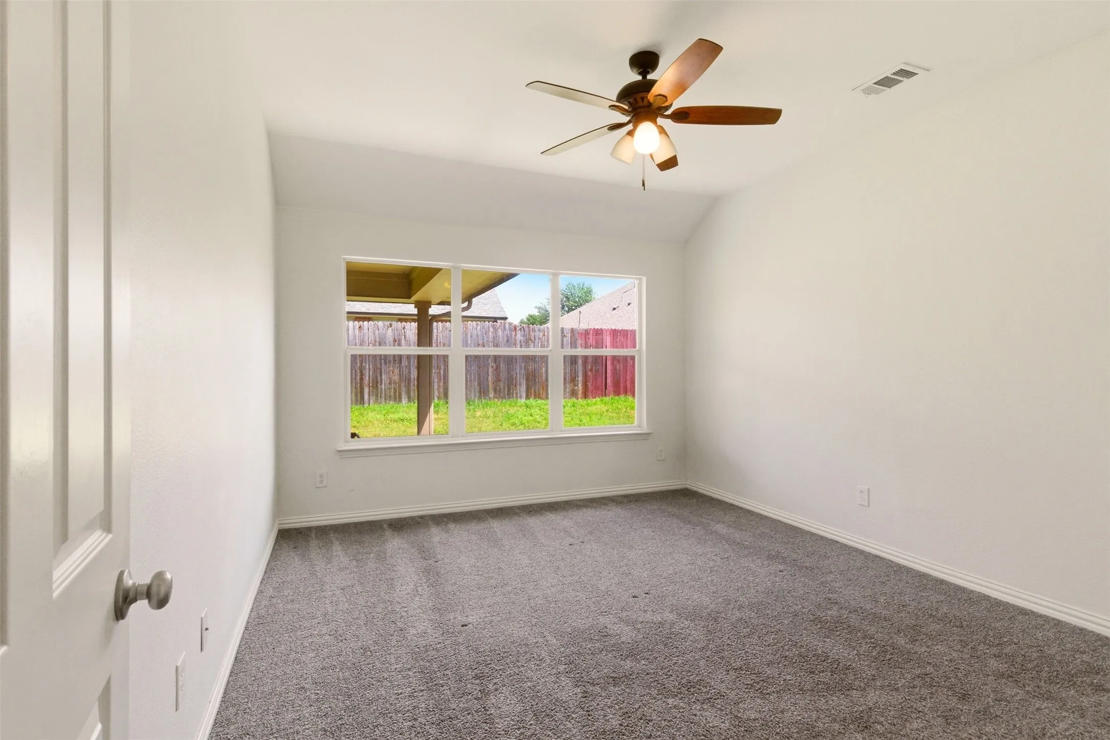 Vaulted ceiling with a ceiling fan, gray carpeting, white walls, and a multi-pane window
