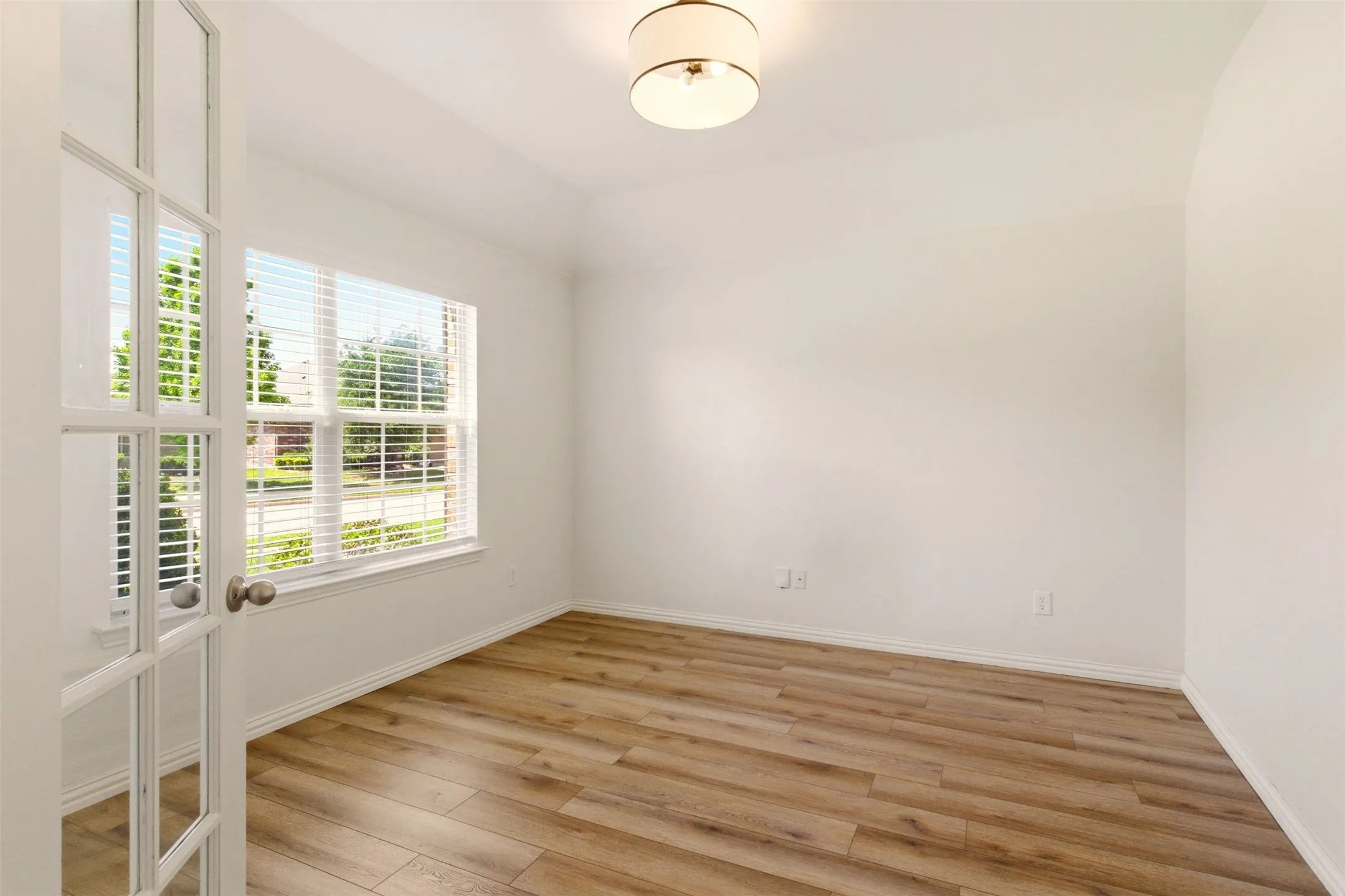 French doors, wood-finish flooring, large window with blinds, ceiling-mounted light fixture, white walls