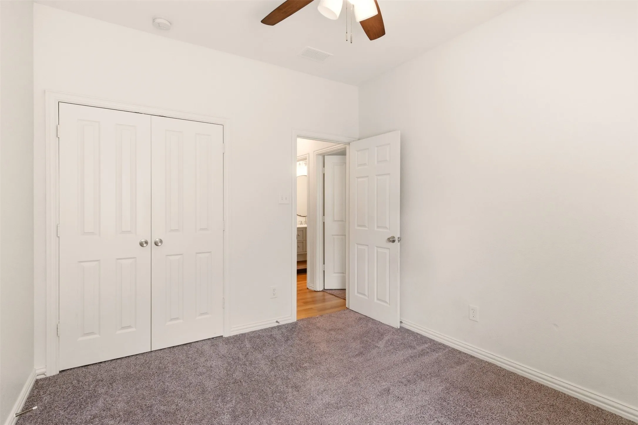 Carpeted room with a ceiling fan, white walls, and a double-door closet