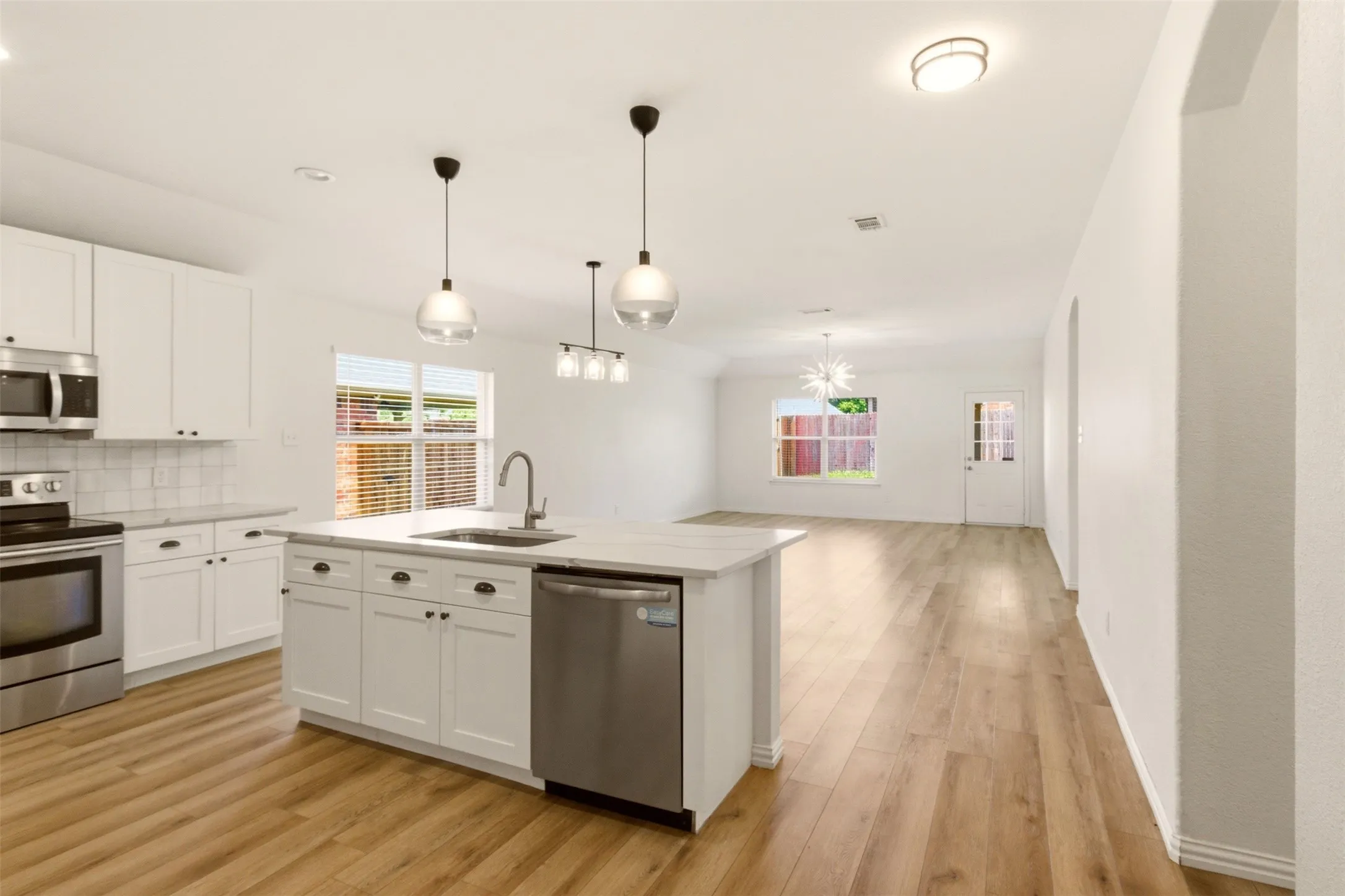 Open-concept kitchen with a central island, stainless steel appliances, white cabinetry, and wood-finish flooring throughout