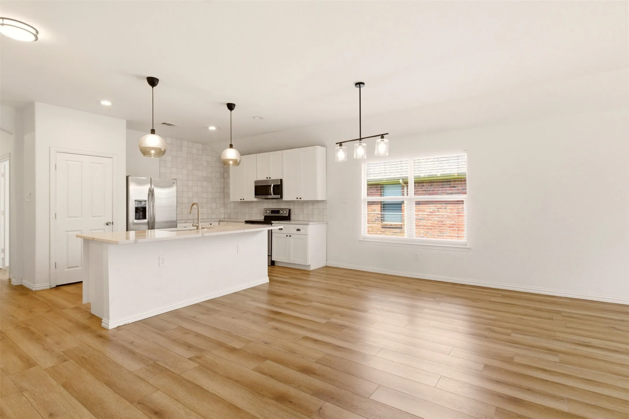 Open-concept living area with wood-finish flooring, a kitchen island, white cabinetry, and stainless steel appliances
