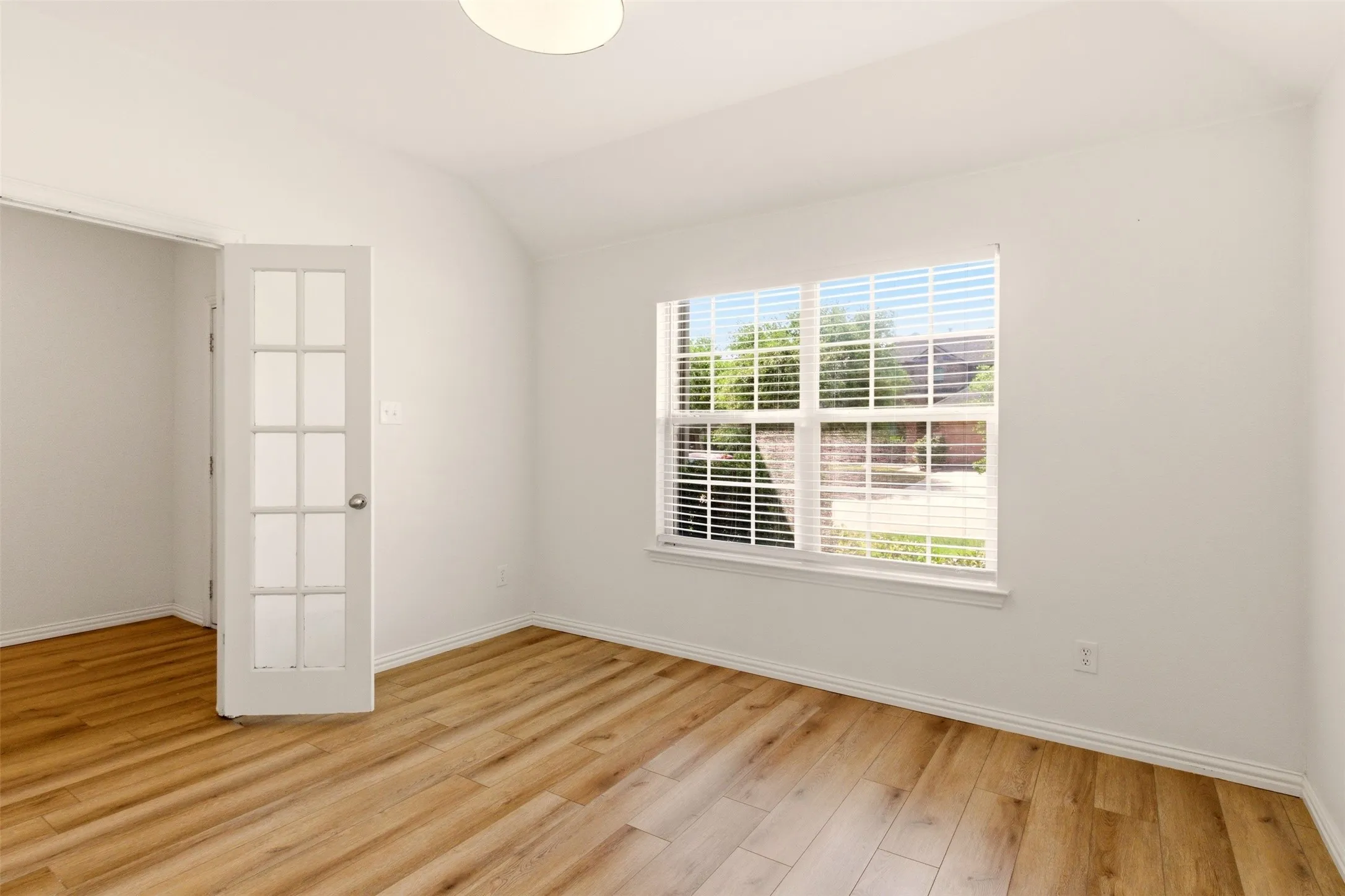 Room featuring wood-finish flooring, a window with horizontal blinds, a ceiling-mounted light fixture, and a French-style door