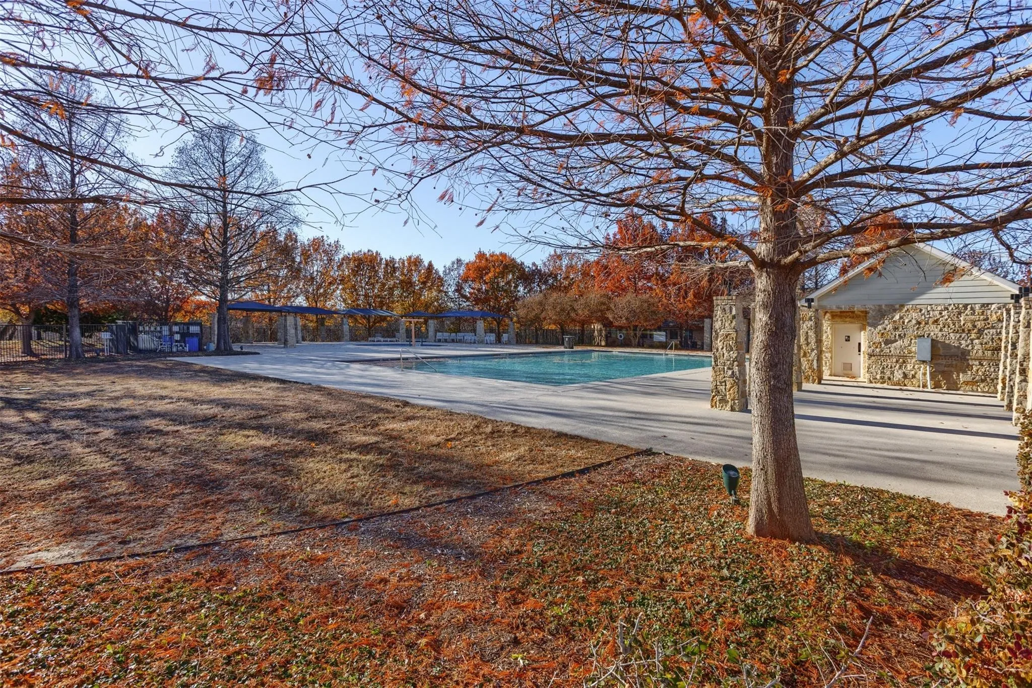 Expansive outdoor pool area featuring a rectangular pool, concrete decking, and a stone-clad building with a gabled roof