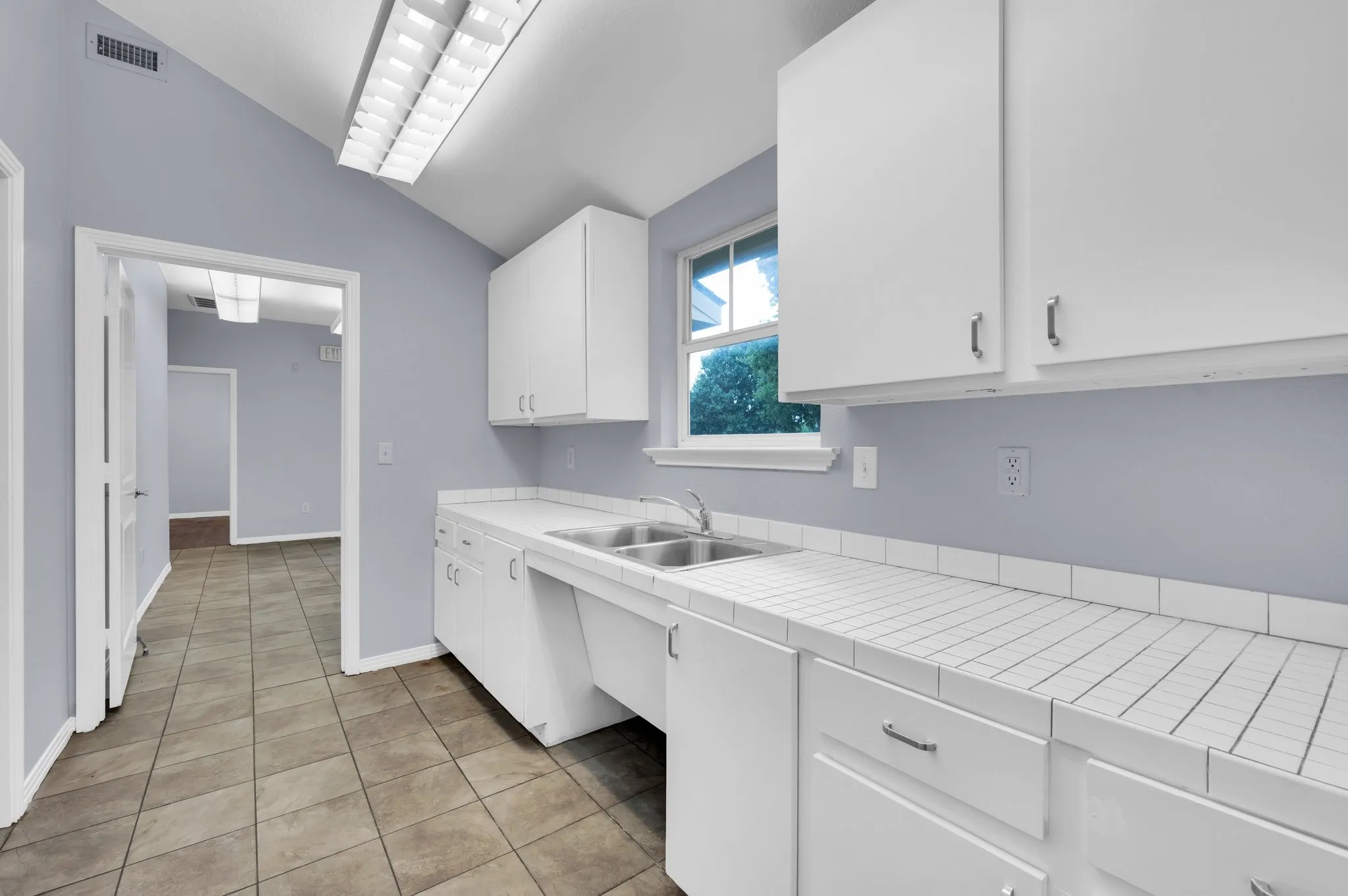 Tile flooring, vaulted ceiling, white cabinetry, double basin sink, and tile countertops