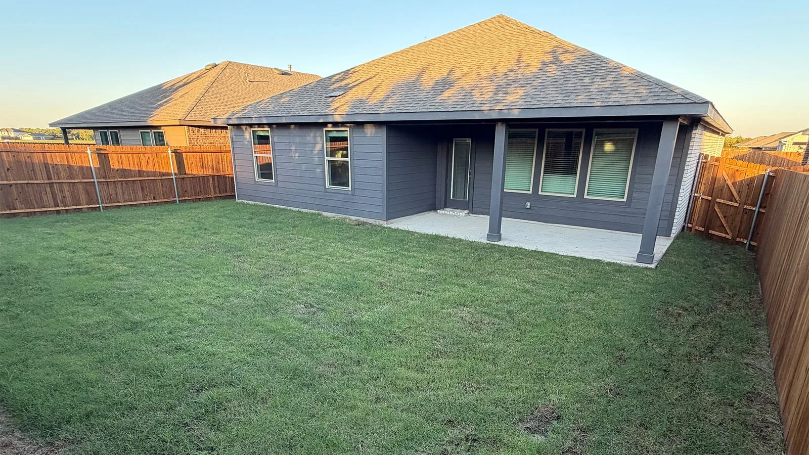 Expansive grassy yard area featuring a covered patio, privacy fencing, and exterior siding