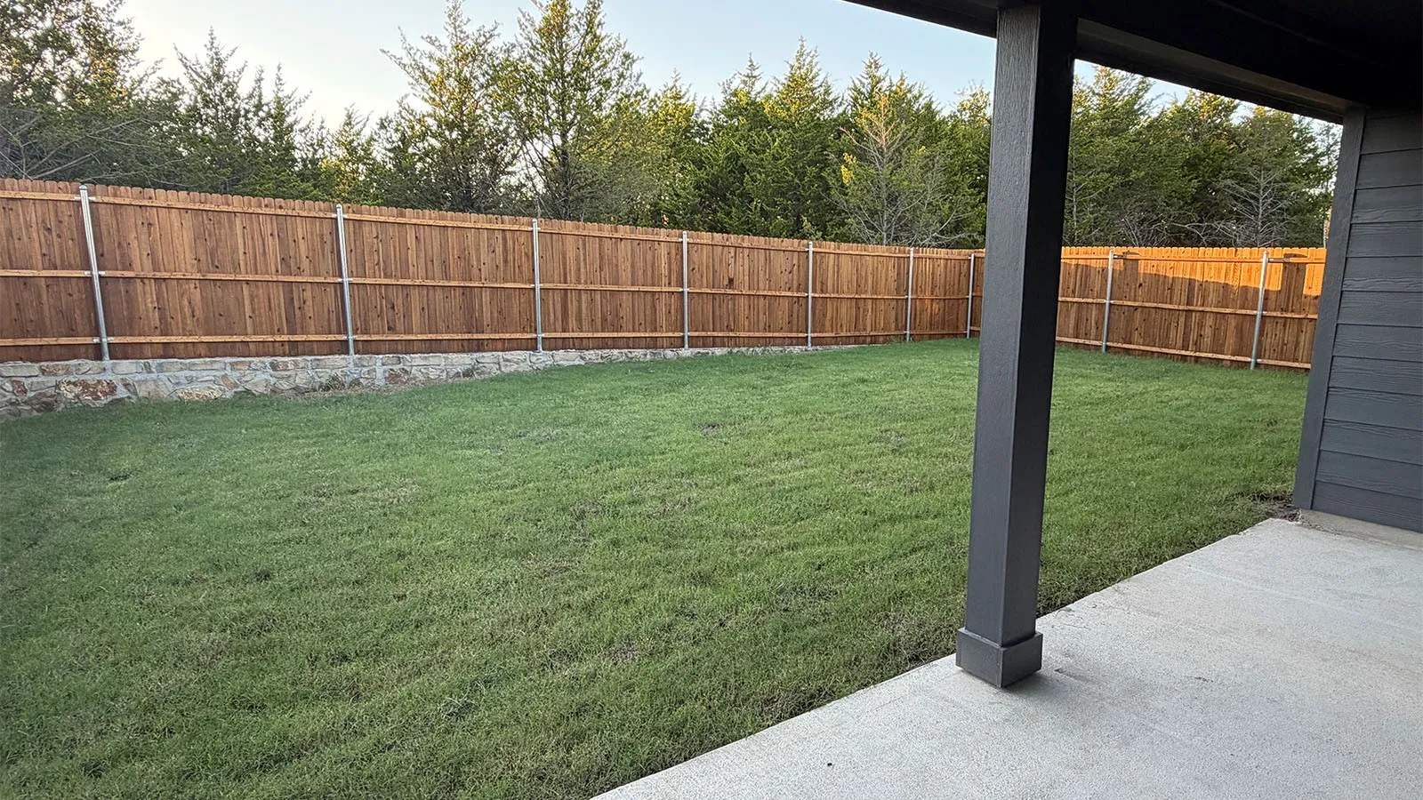 Expansive grassy yard with a wood fence featuring a stone base