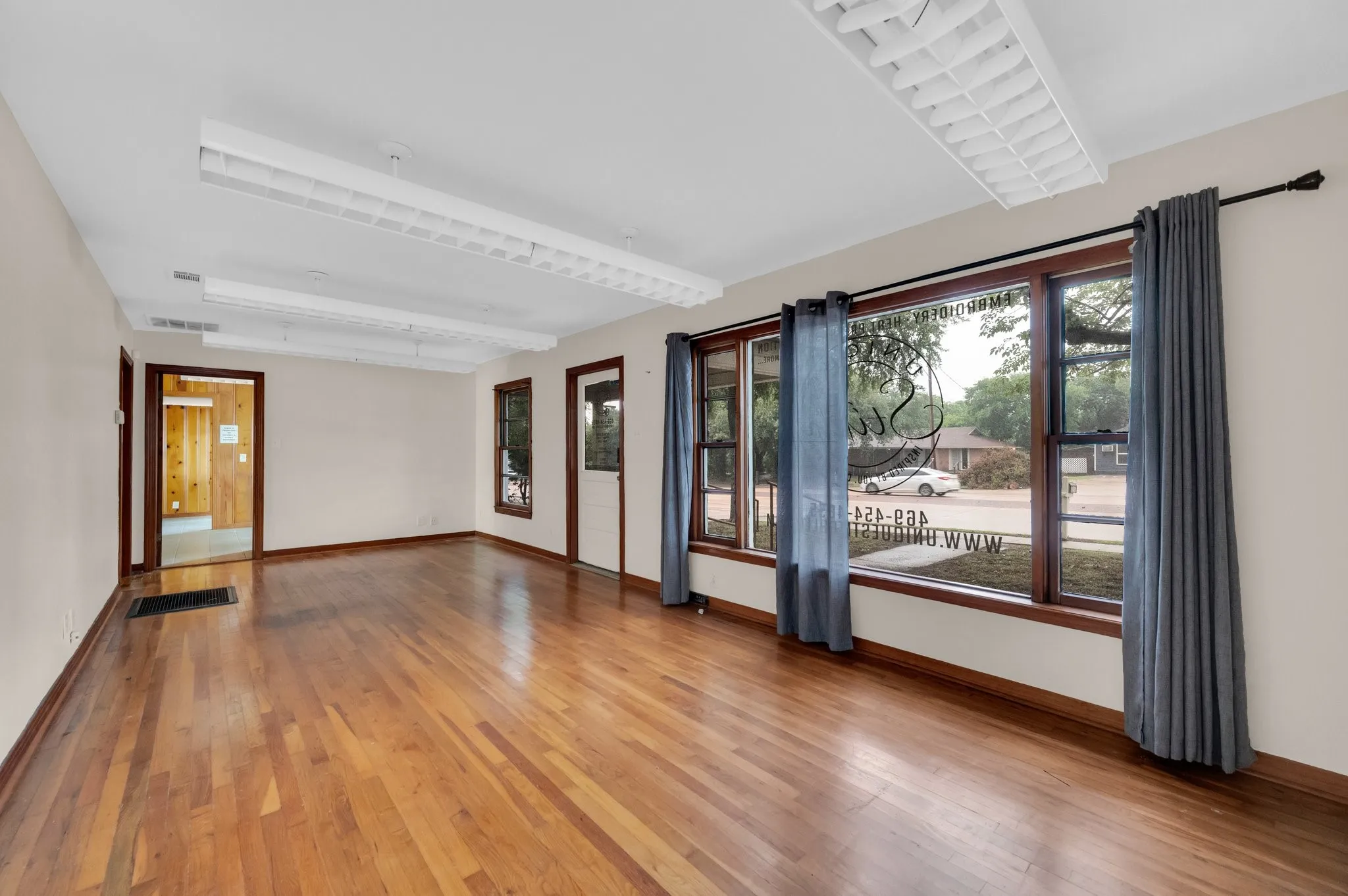 Hardwood flooring with a gloss finish, multiple windows with wood trim, and overhead fluorescent lighting fixtures