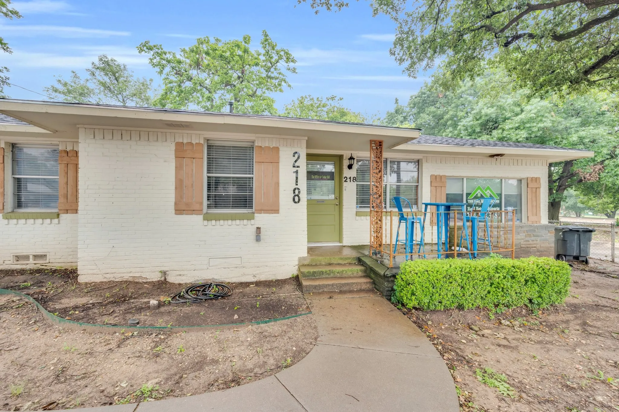 White brick exterior with wood-tone shutters, a sage green door, and a concrete pathway leading to the entrance