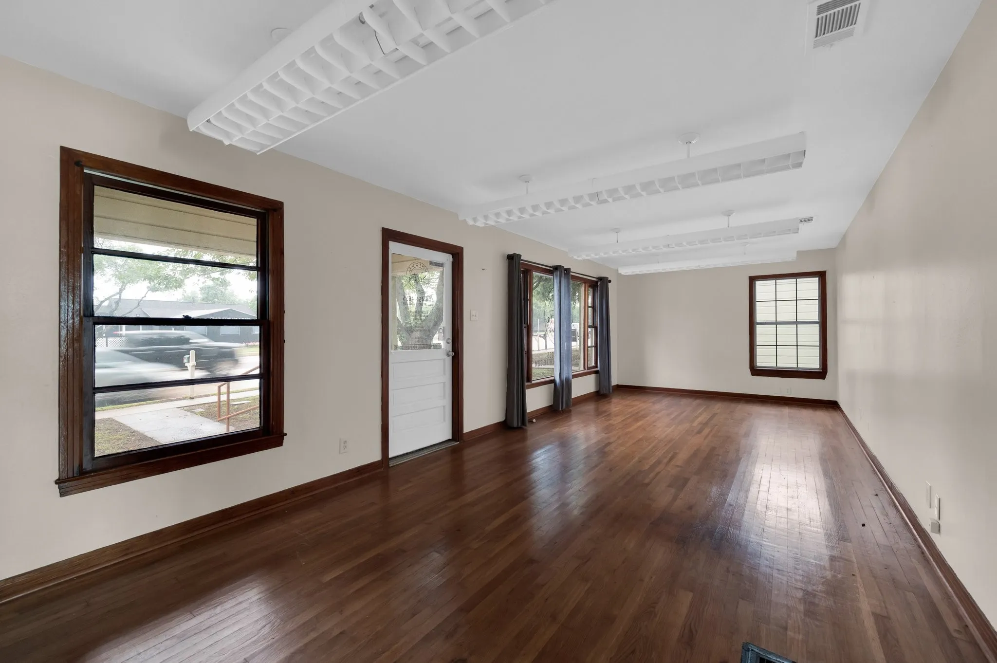 Hardwood flooring, multiple windows with dark wood trim, white walls, white ceiling with integrated lighting, and a white paneled door