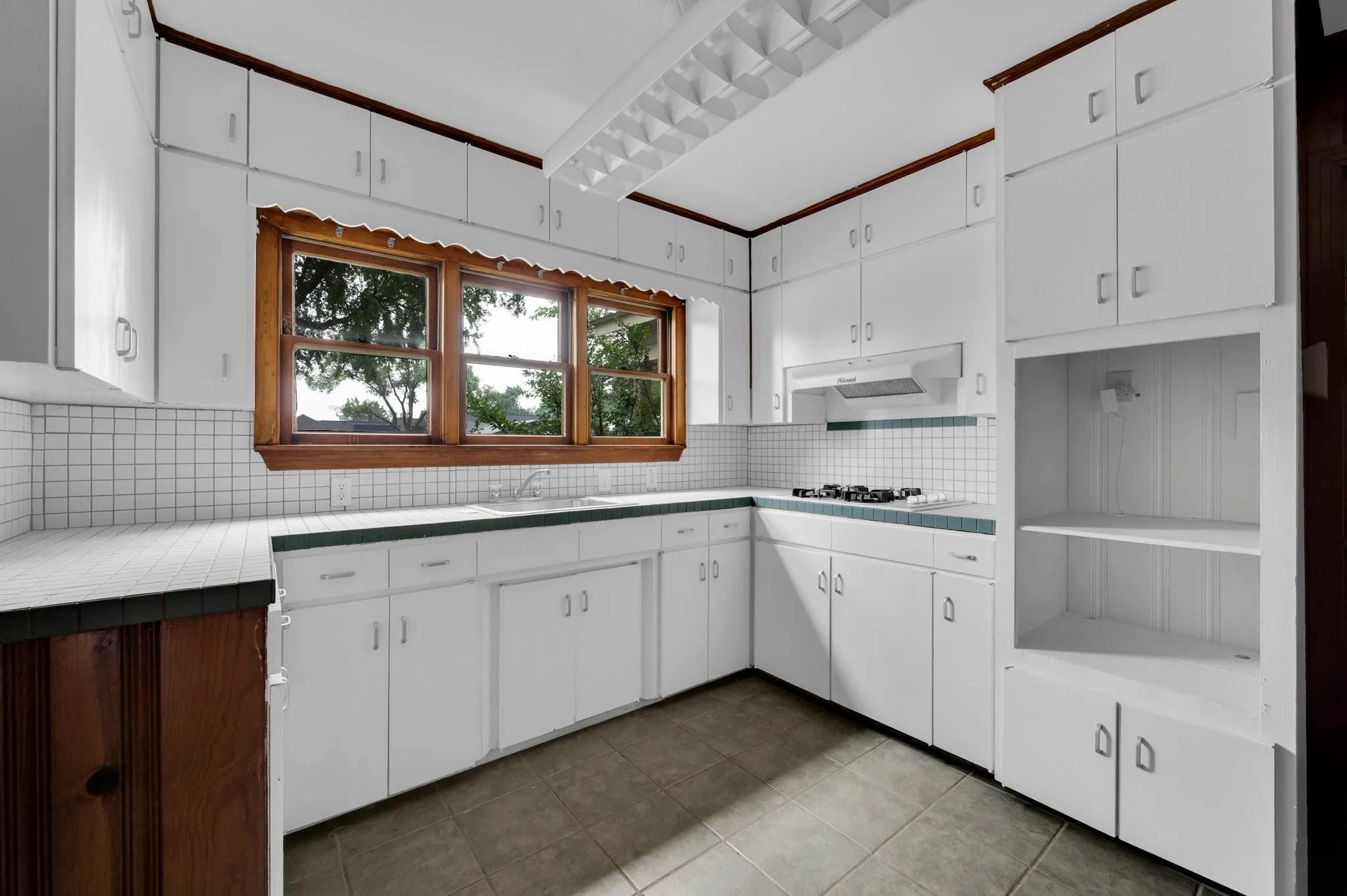 White cabinetry with abundant storage, wood-frame windows, tiled countertops, and a four-burner gas range