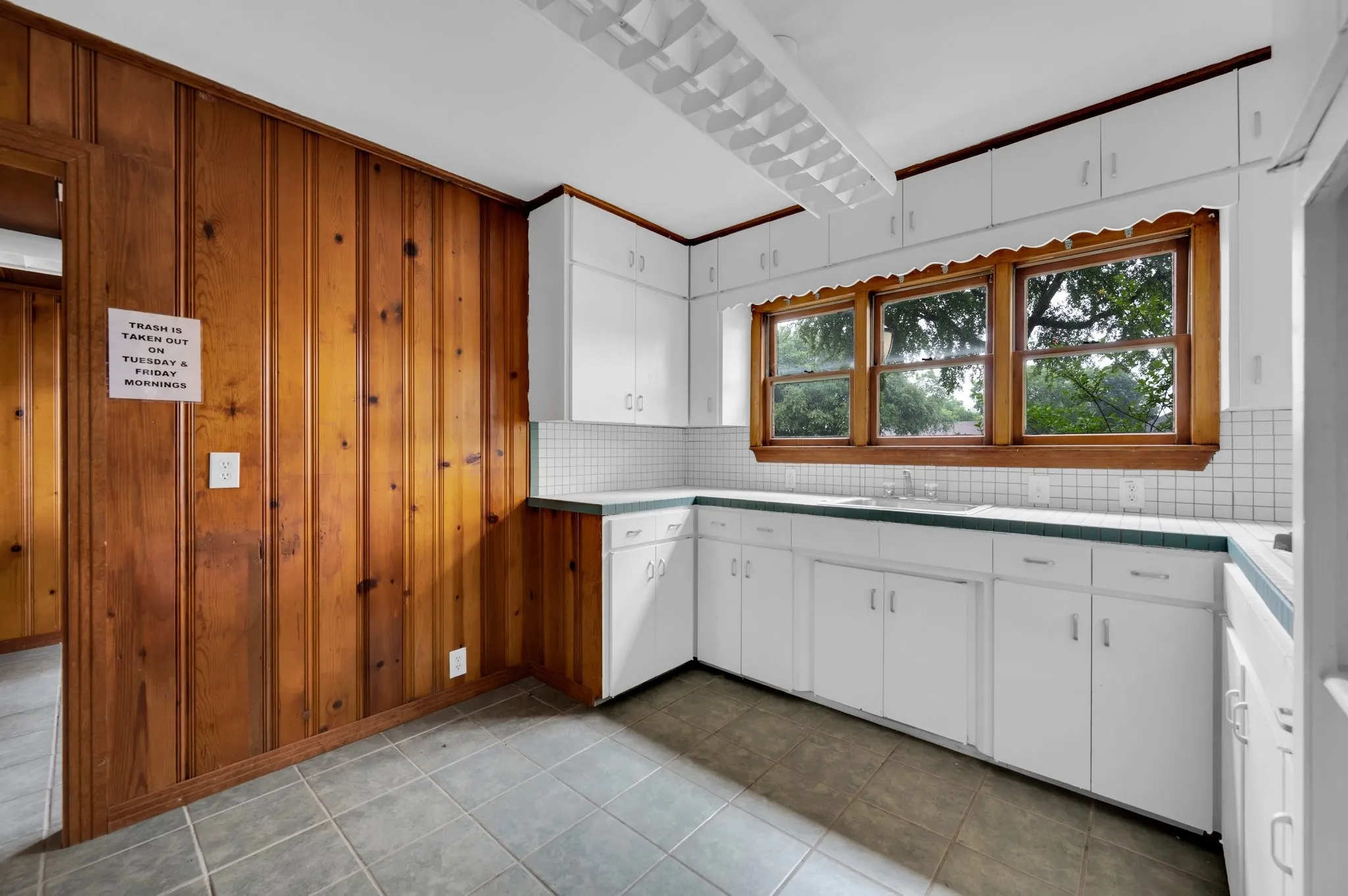 White cabinetry, wood paneling, tiled flooring, white subway tile backsplash, and a multi-pane window