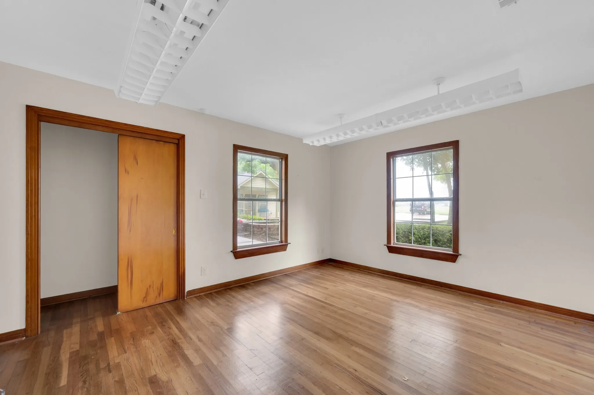 Hardwood flooring throughout, two windows with wood trim, wood-paneled pocket door, and two ceiling-mounted light fixtures