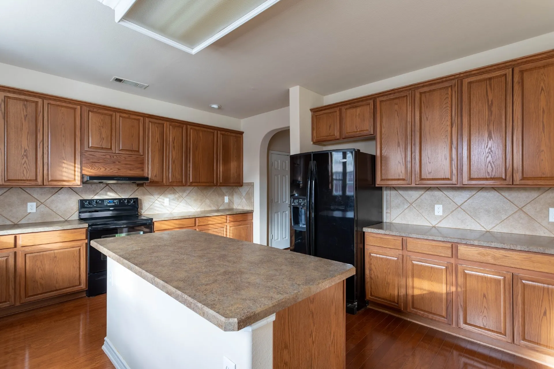 Kitchen featuring wood-finish cabinetry, a central island with a solid surface countertop, tile backsplash, and black appliances