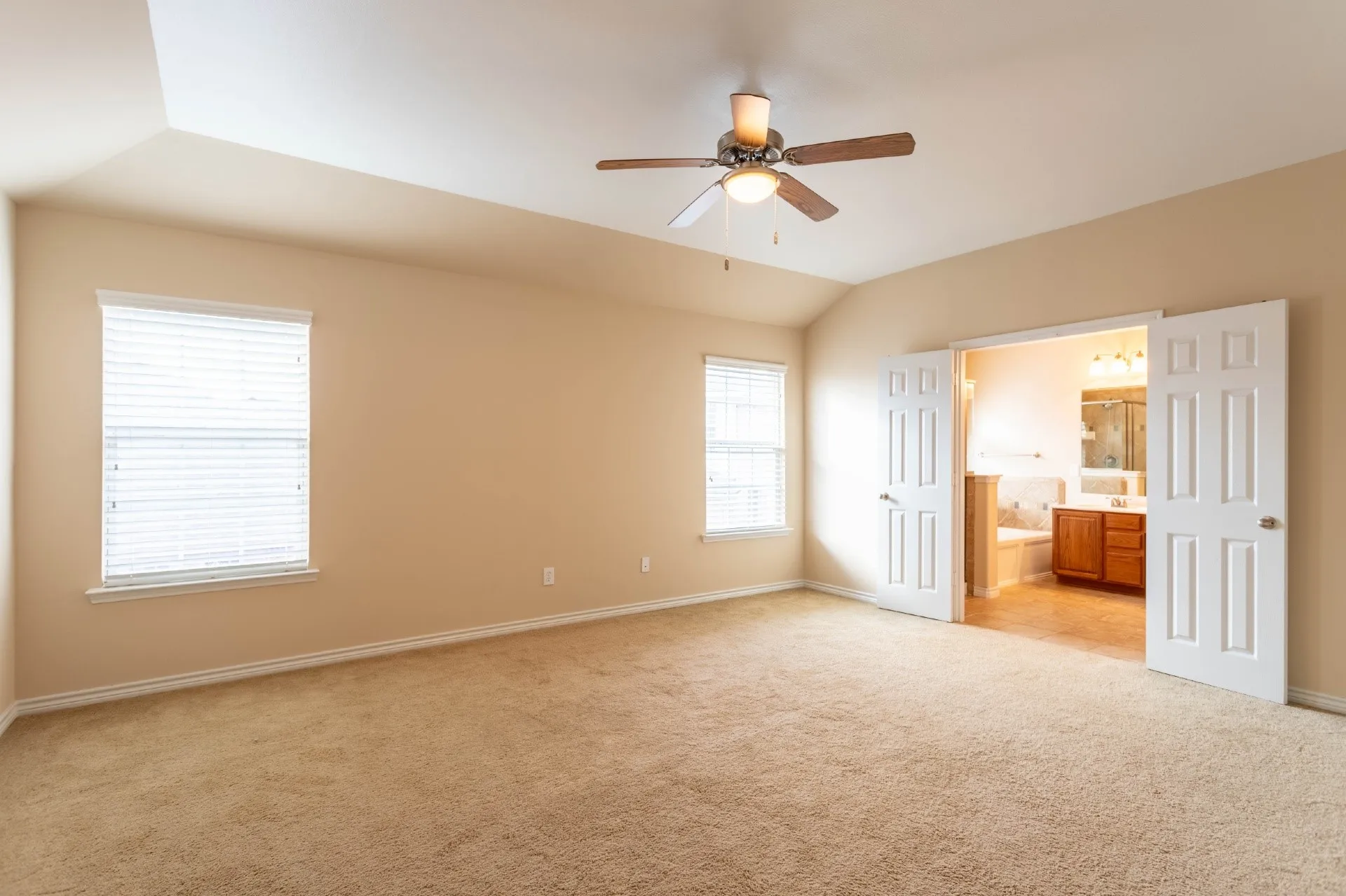 Vaulted ceiling featuring a ceiling fan, two windows with blinds, and carpeted flooring