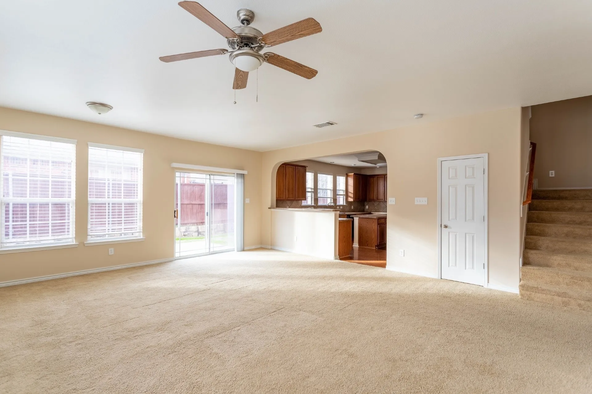 Spacious living area featuring carpet flooring, ceiling fan, and multiple windows with blinds
