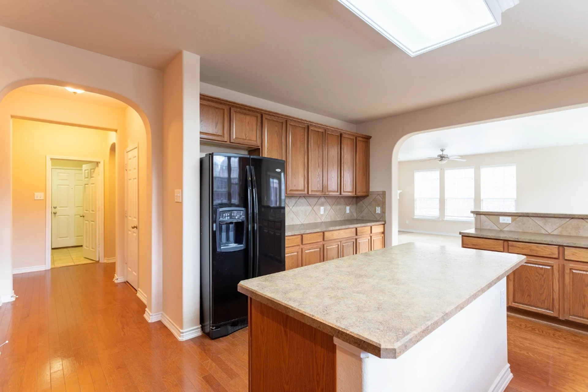 Kitchen featuring wood-finish flooring, a central island with a solid surface countertop, wood cabinetry, and a tile backsplash