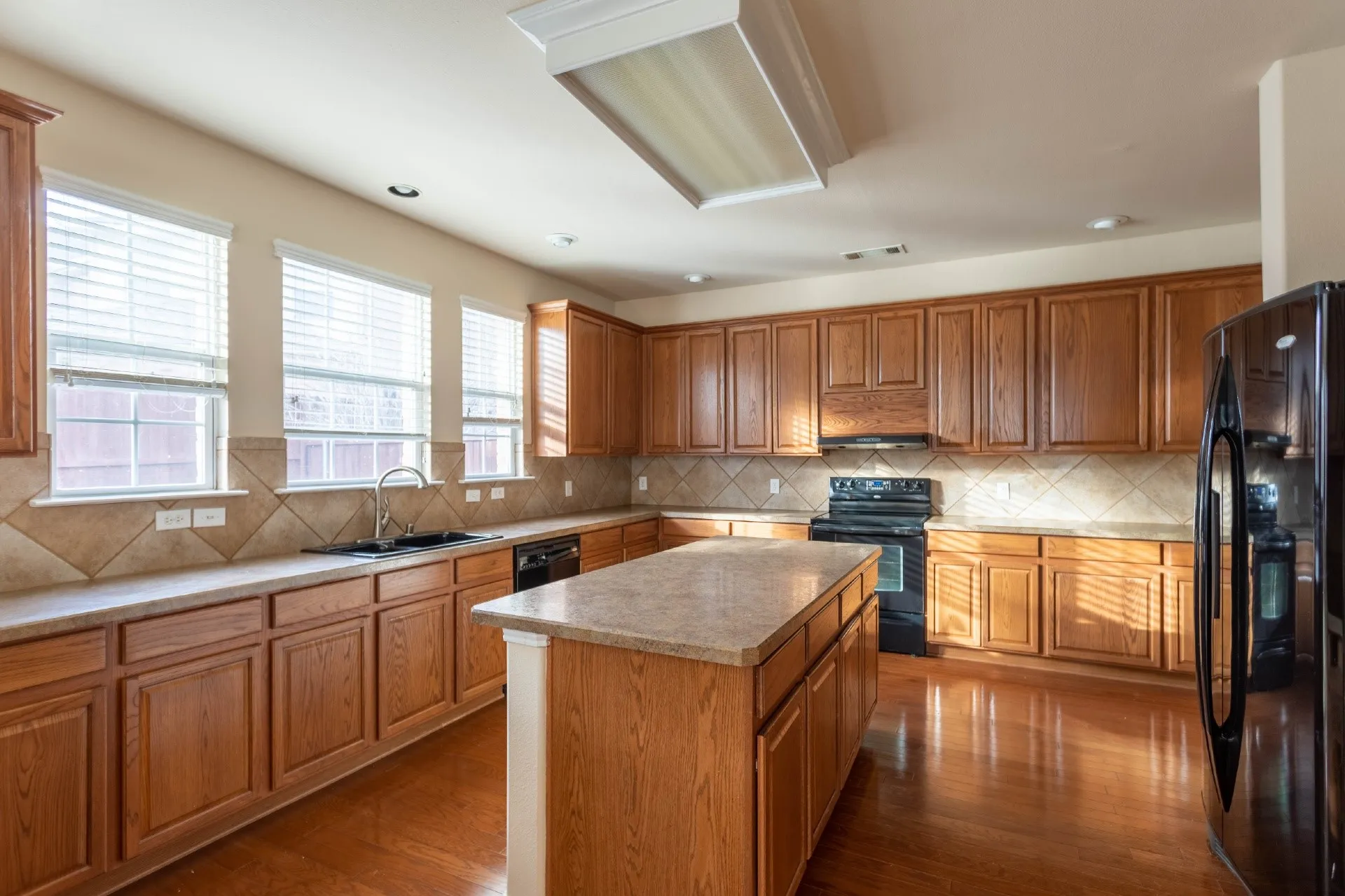 Kitchen featuring wood-finish flooring, wood cabinetry, granite-style countertops, a large center island, and a black appliance suite