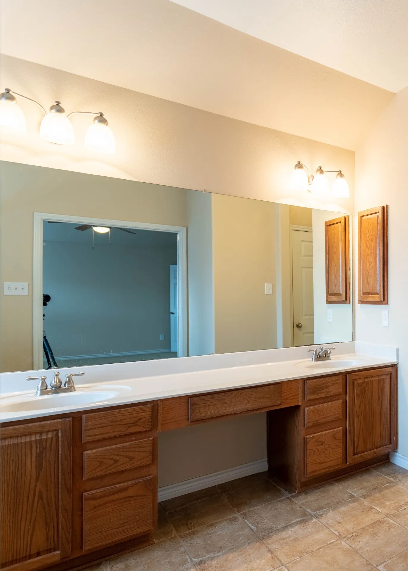 Dual vanity with undermount sinks and chrome fixtures, expansive wall-mounted mirror, wood-finish cabinetry, and tiled flooring