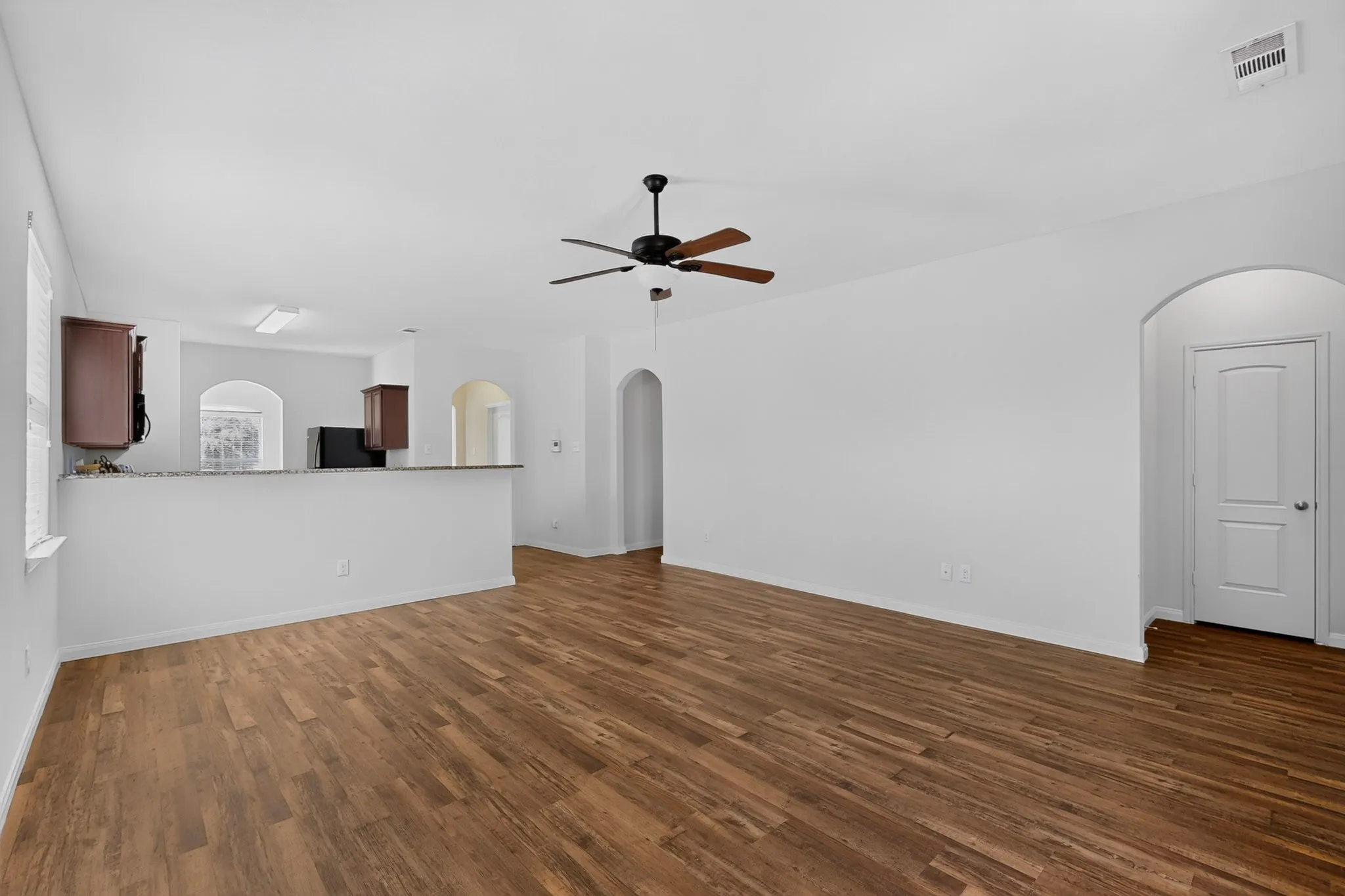 Open-concept living area with wood-finish flooring, a ceiling fan, and arched doorways