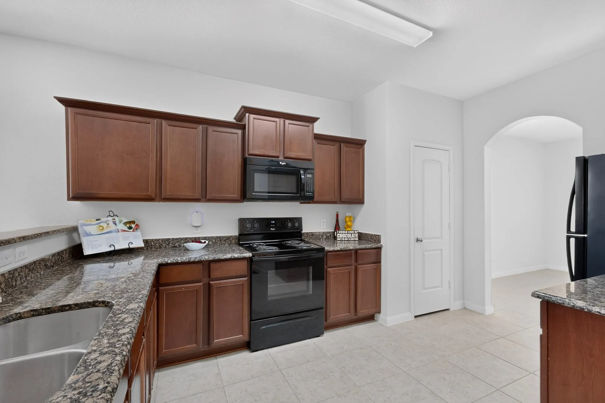 Kitchen featuring granite-style countertops, wood-finish cabinetry, stainless steel sink, and tile flooring