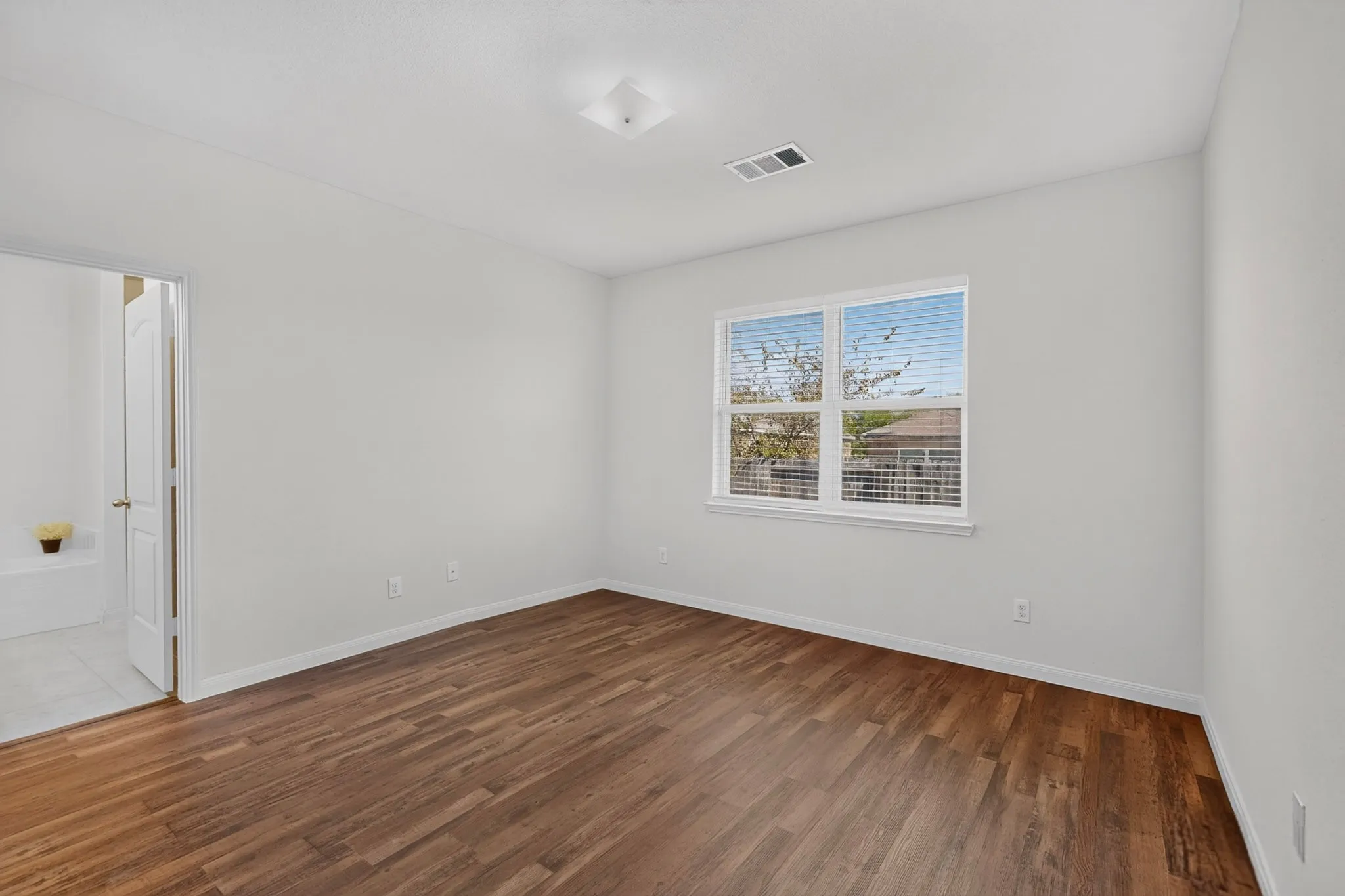 Wood-finish flooring, white walls, and a window with blinds