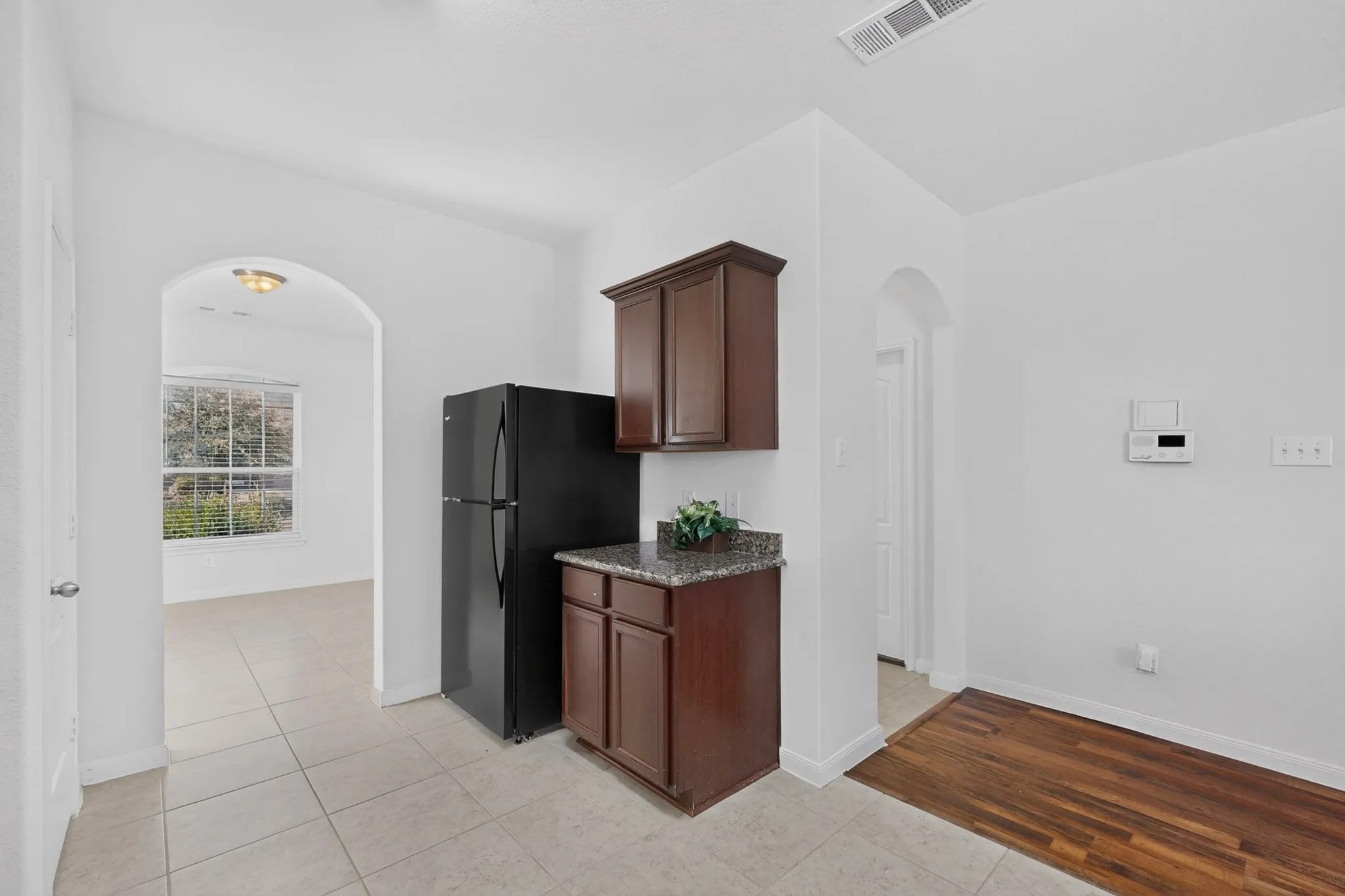 Arched doorway, tile flooring, wood-finish flooring, dark wood cabinetry, and a granite-finish countertop