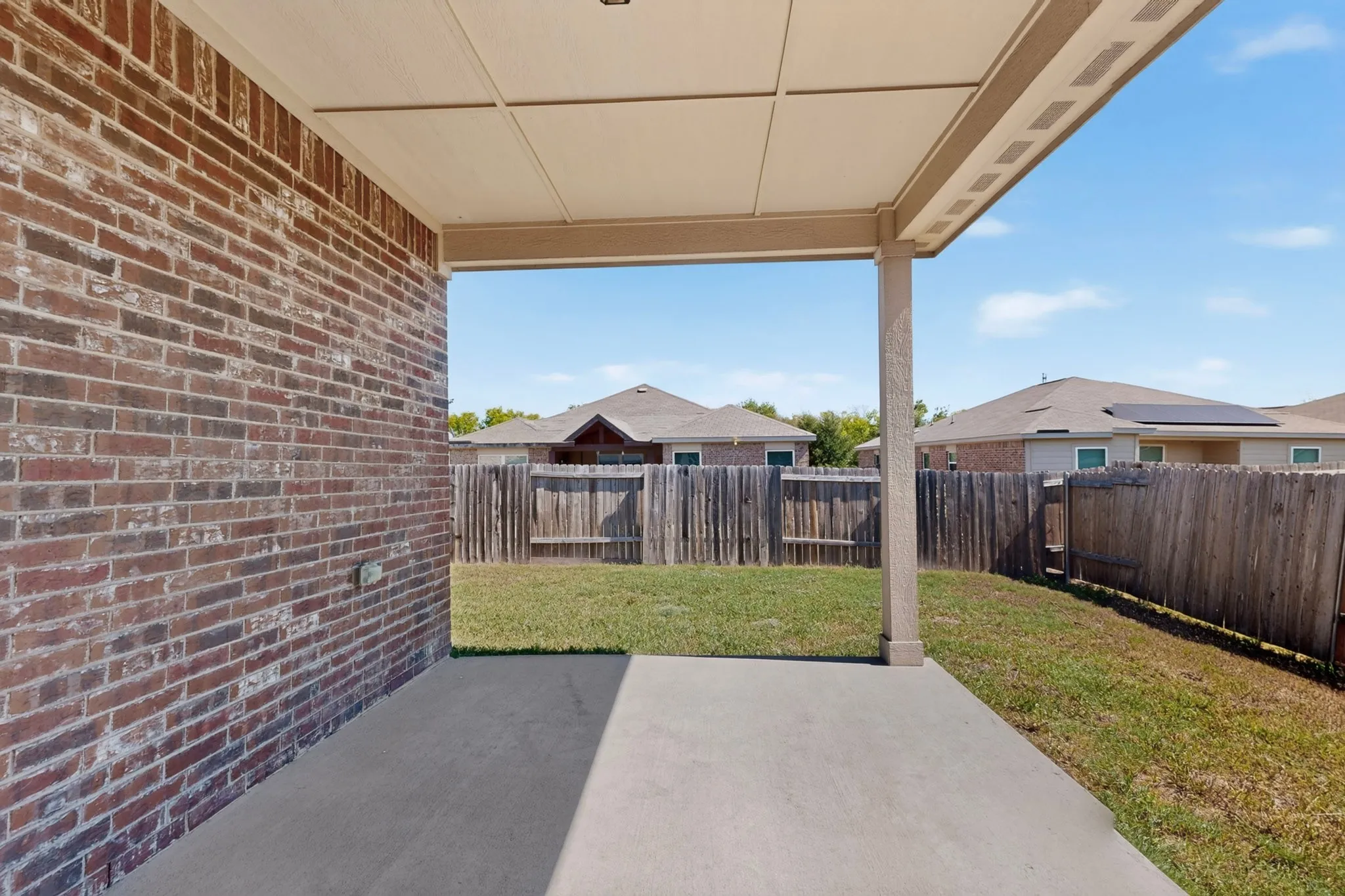 Covered patio with a concrete slab, brick exterior, and a fenced backyard