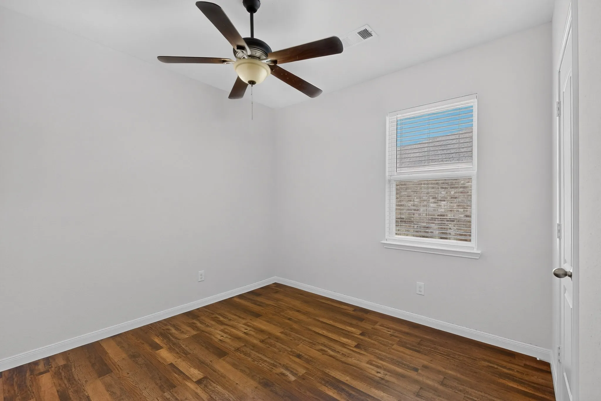 Wood-finish flooring, ceiling fan with integrated lighting, white trim, and a white interior door