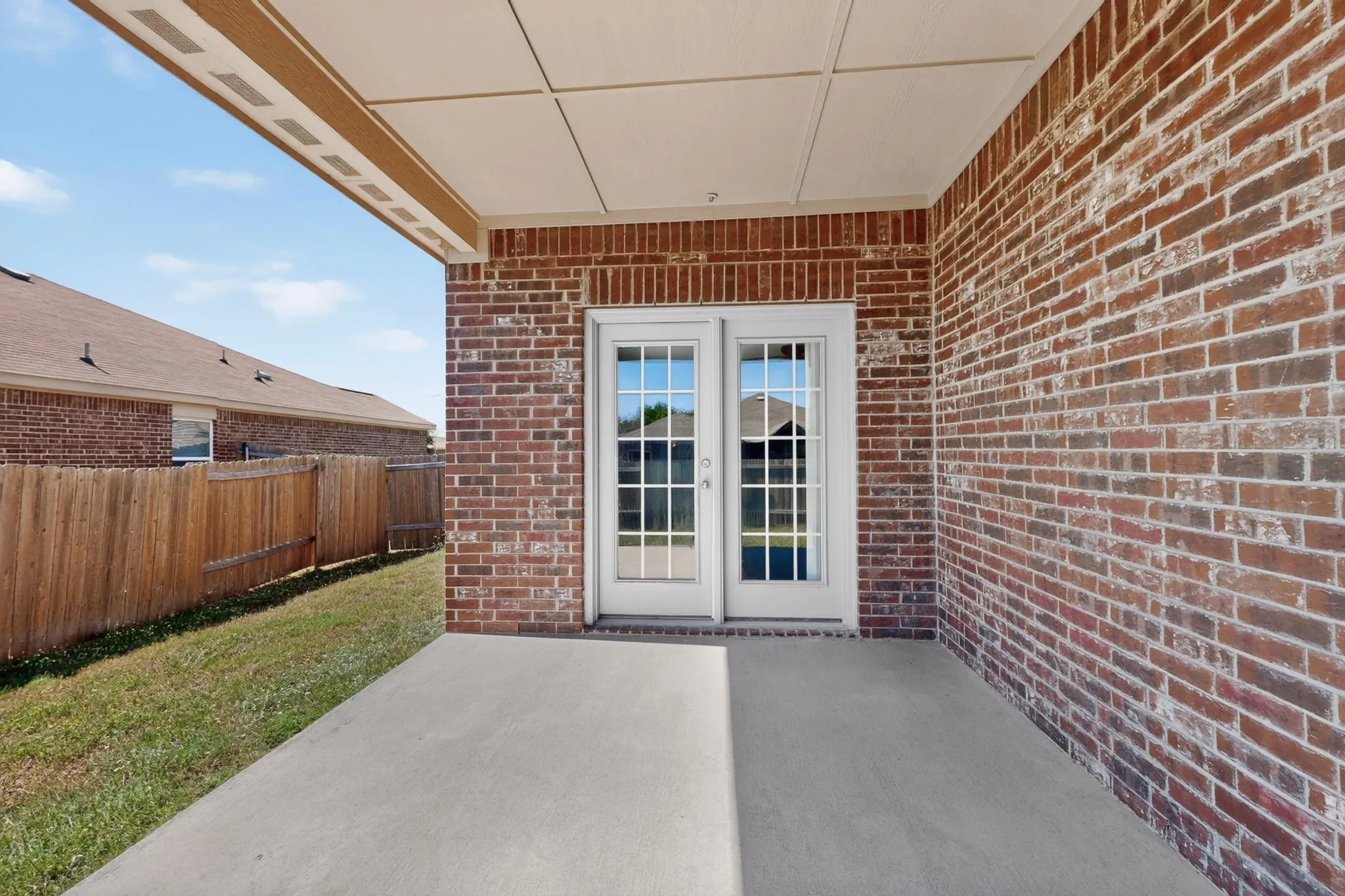 Brick exterior with covered patio, concrete surface, and French doors