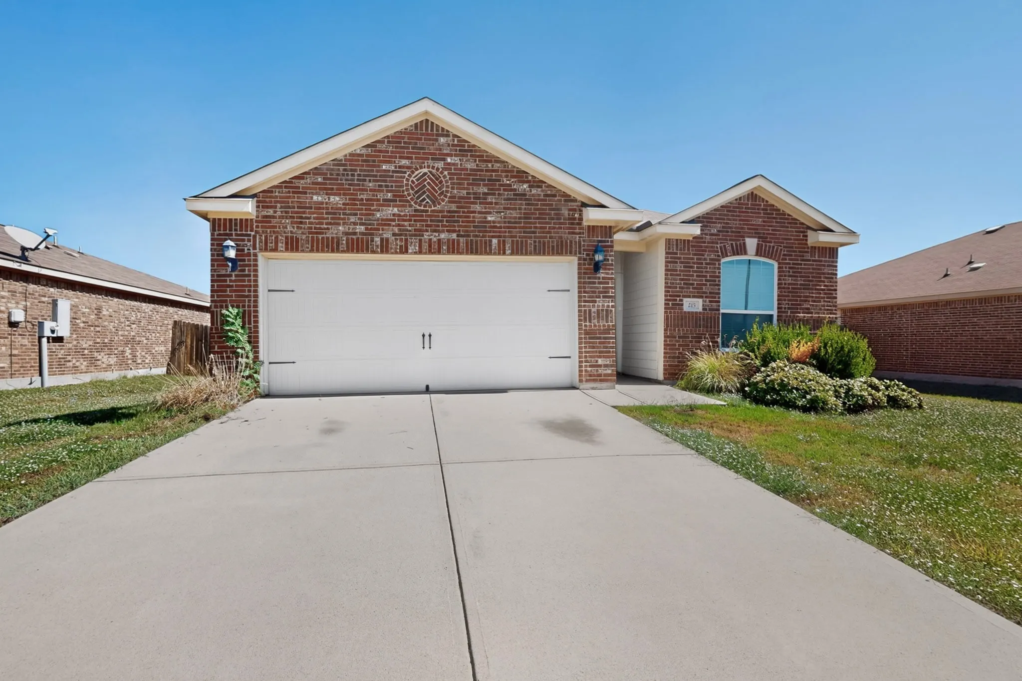 Welcoming brick exterior with a white two-car garage door, complemented by manicured landscaping and a concrete driveway