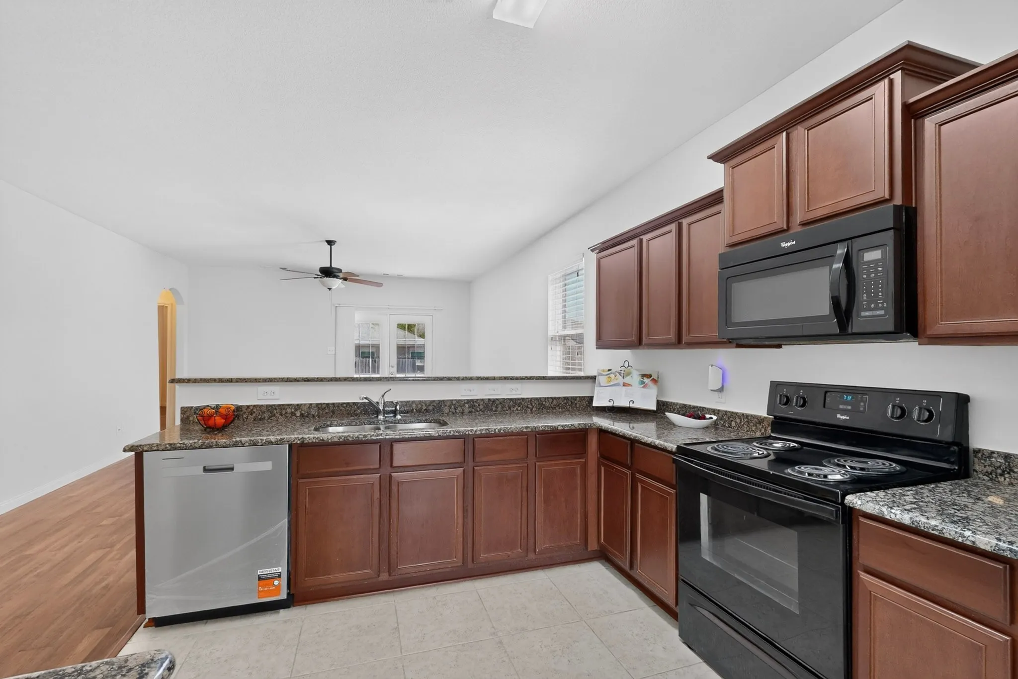 Kitchen featuring wood-finish cabinetry, granite countertops, tile flooring, and integrated black appliances