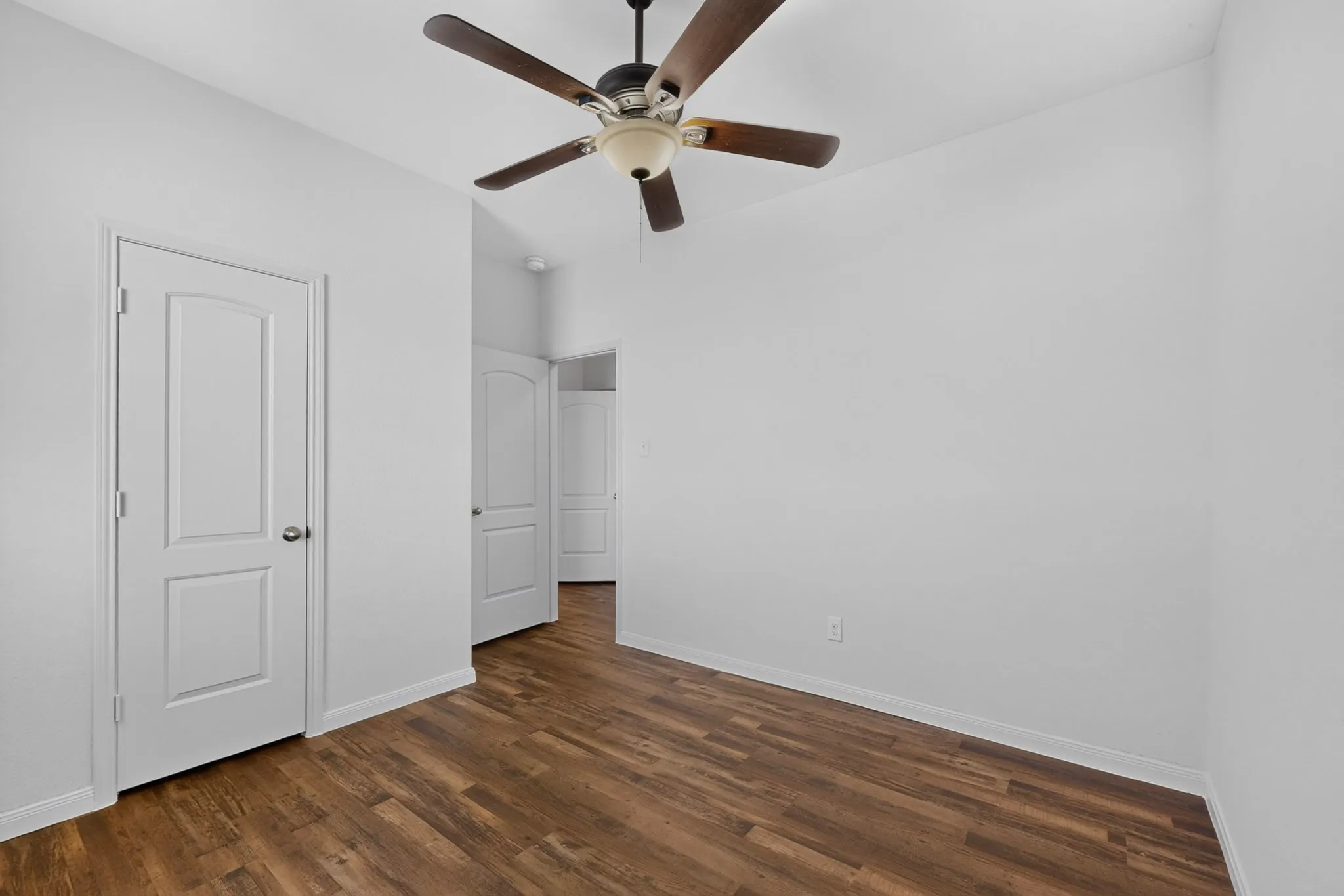 Wood-finish flooring with white baseboards, a ceiling fan with light fixture, and white interior doors with satin nickel hardware