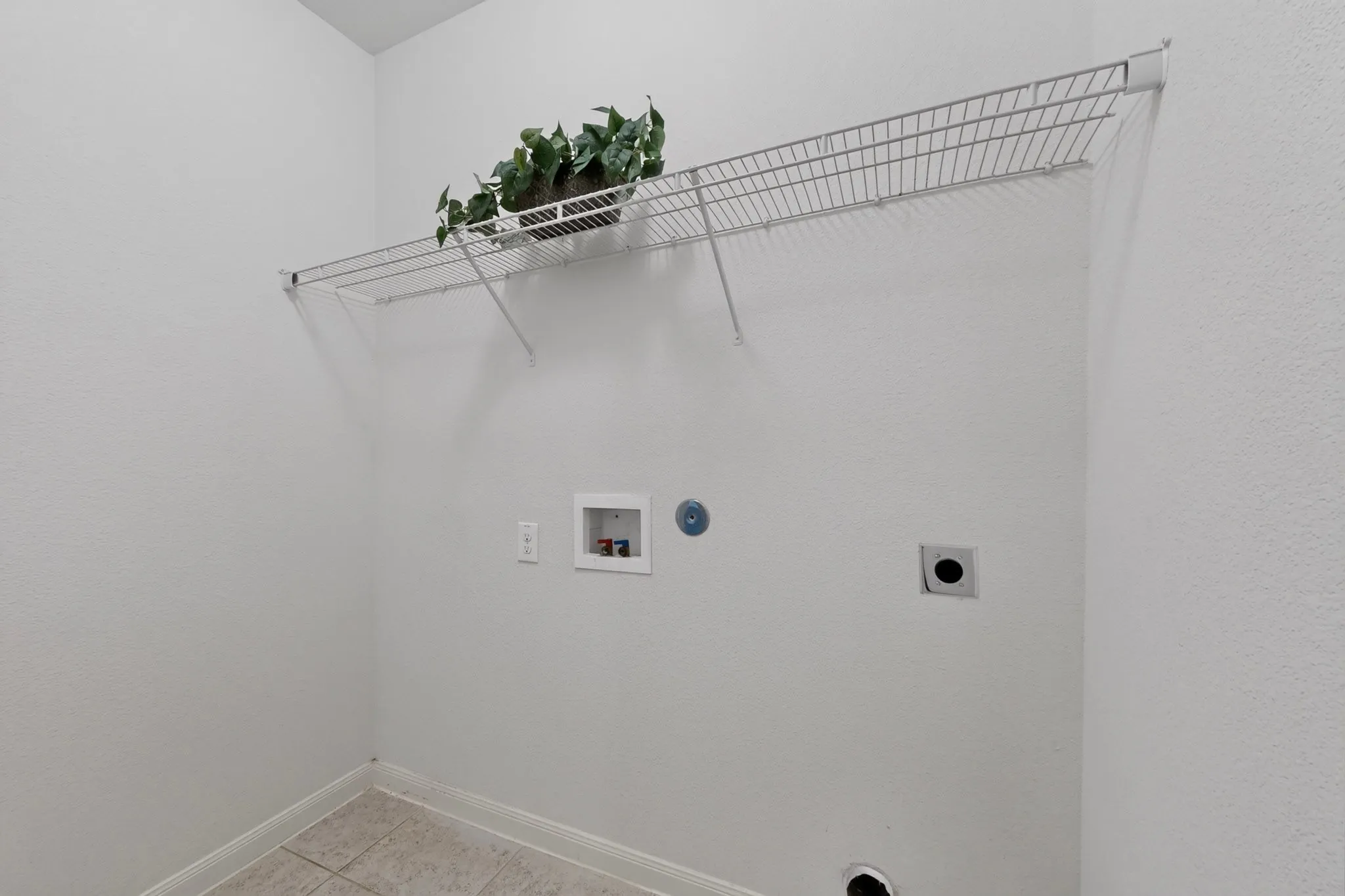 White wire shelving unit over utility hookups, complemented by light-toned tile flooring