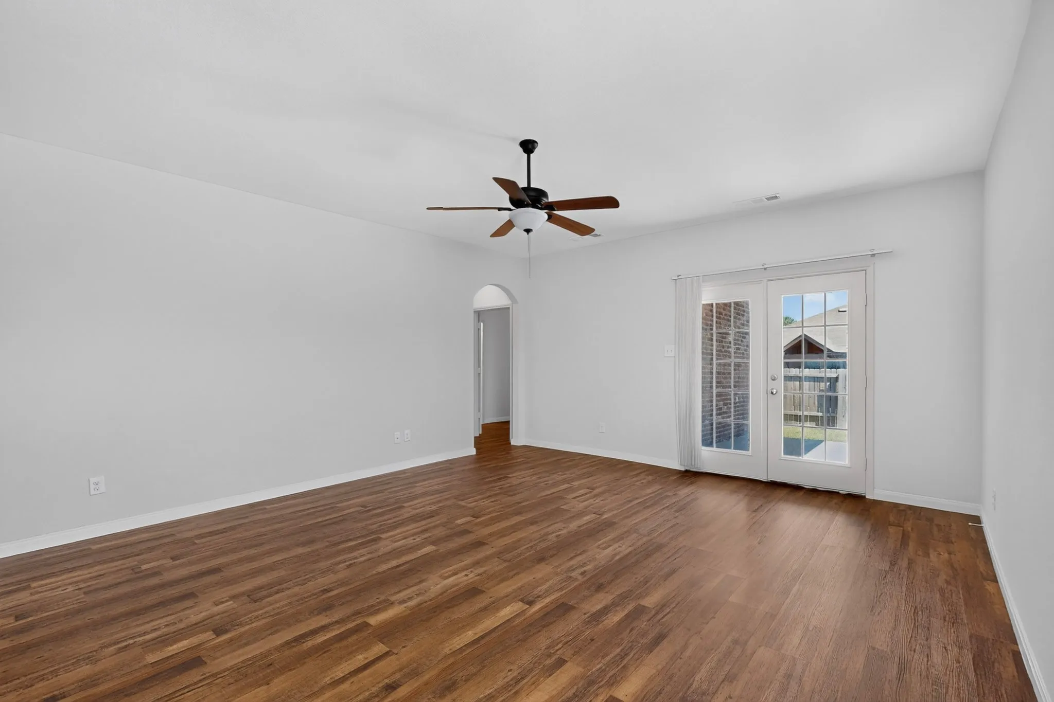 Spacious room with wood-finish flooring, ceiling fan, and white walls