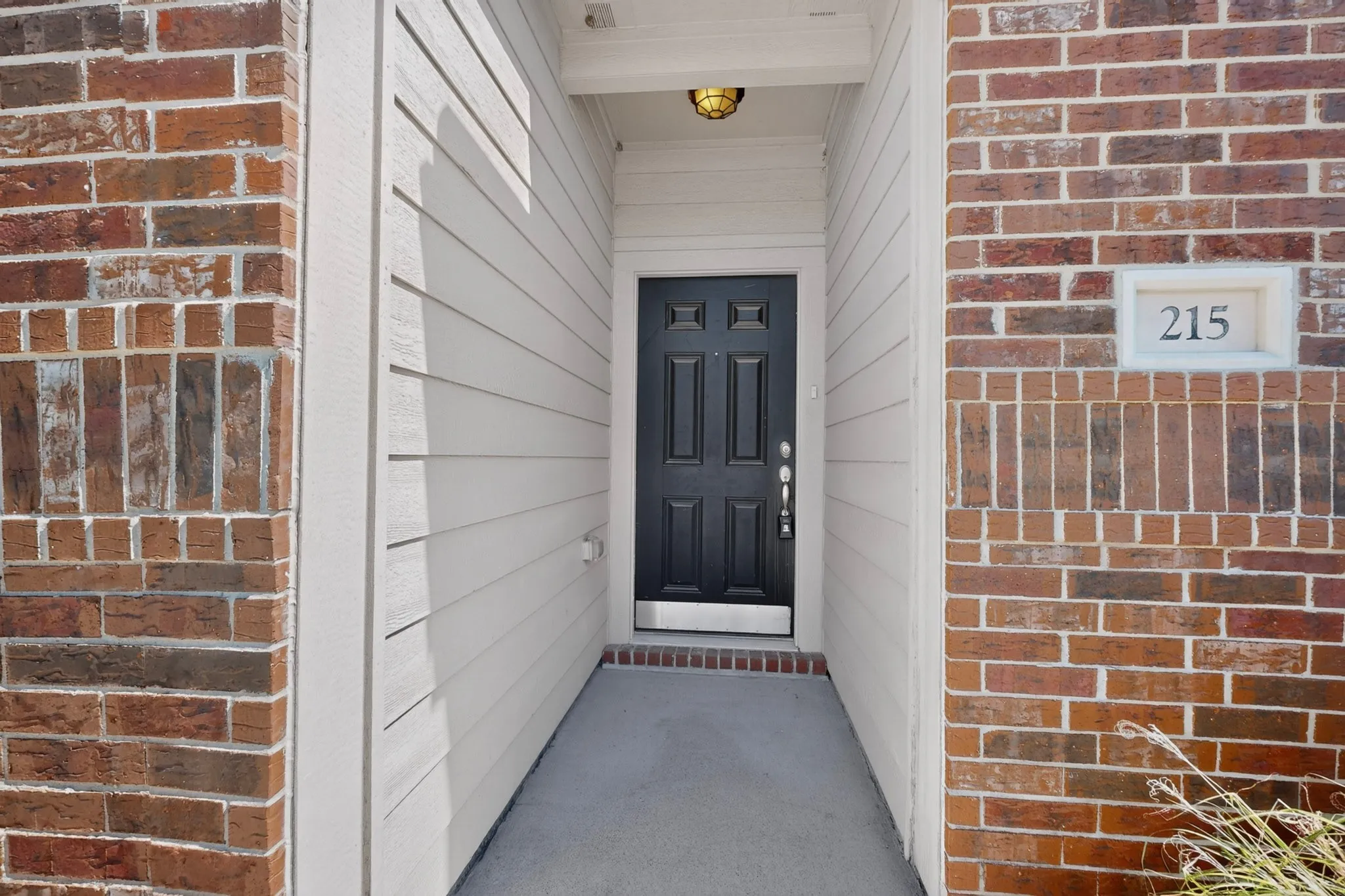 Brick and siding exterior with a paneled entry door, overhead lighting fixture, and visible address number