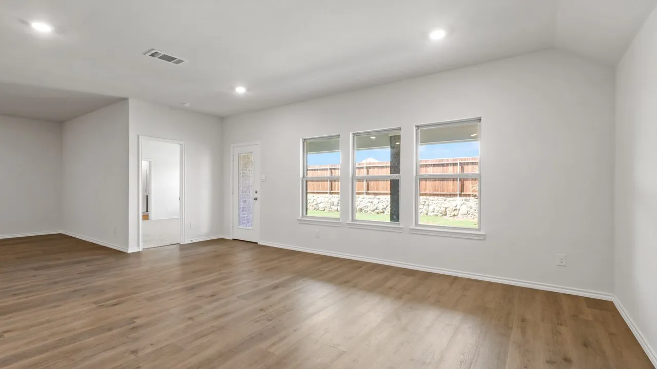 Spacious room featuring wood-finish flooring, white walls, and a vaulted ceiling