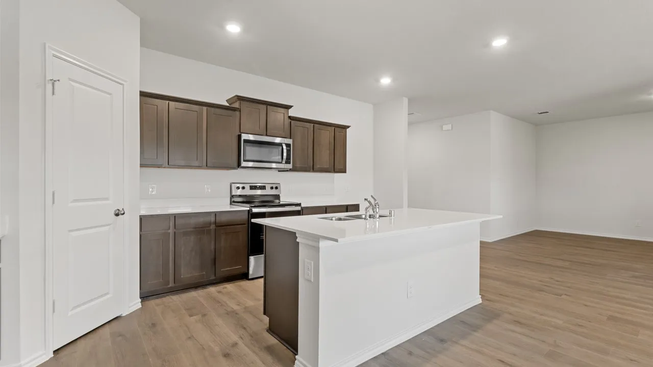 Modern kitchen featuring dark wood cabinetry, white countertops, stainless steel appliances, and a central island with an undermount sink