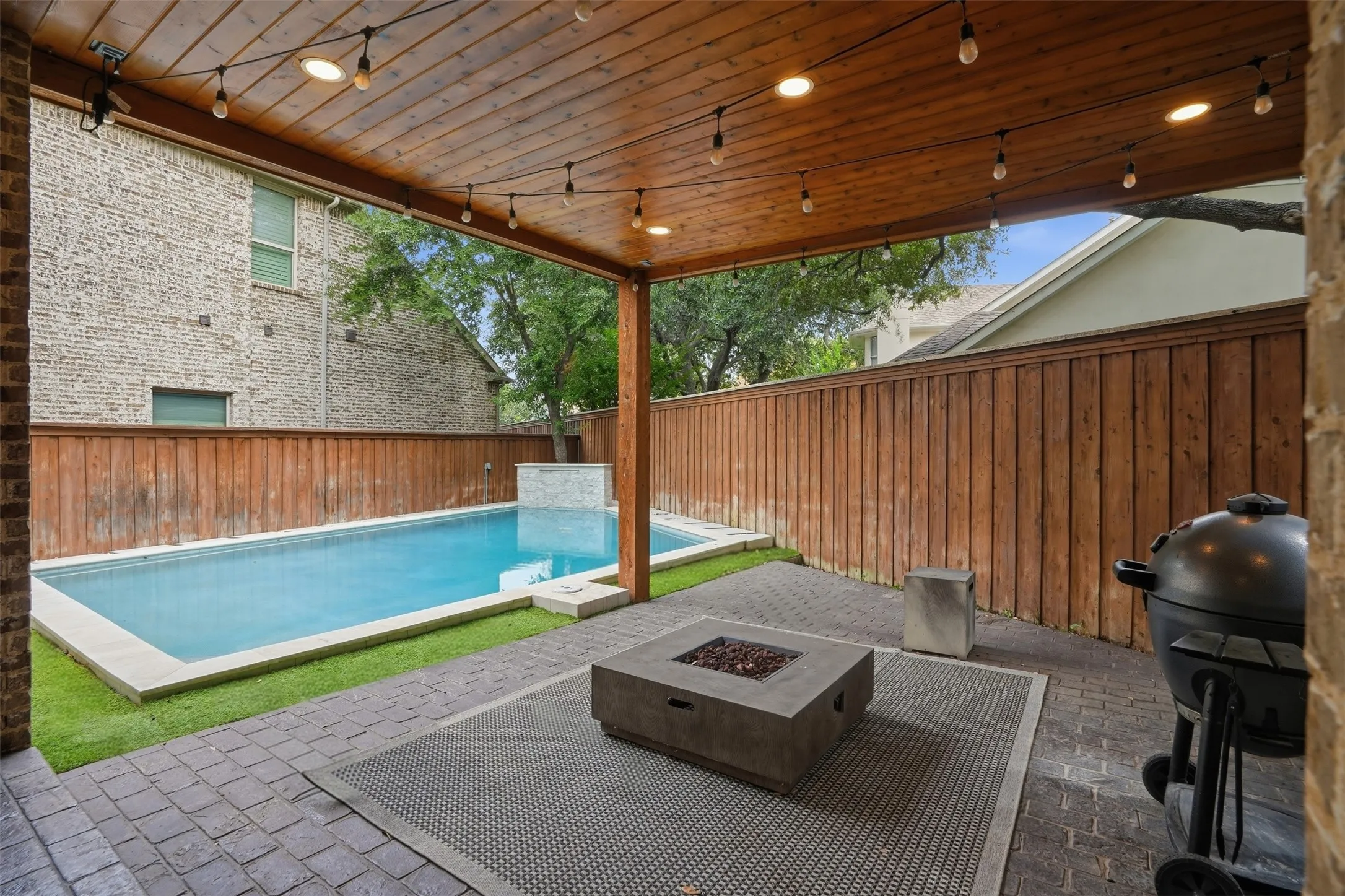 Covered porch with fire pit overlooks the newly added heated pool and turfed yard.