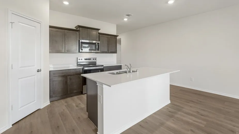 Kitchen featuring an island with an integrated sink, dark wood cabinetry, stainless steel appliances, light countertops, and wood-finish flooring