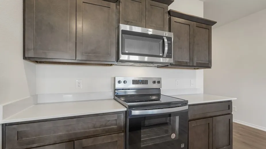 Kitchen featuring dark wood-finish cabinetry, light countertops, a stainless steel microwave, and a black and stainless steel range