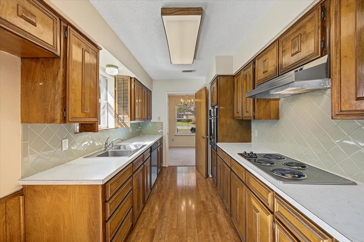 Galley kitchen featuring wood-finish cabinetry, solid surface countertops, and an integrated double oven
