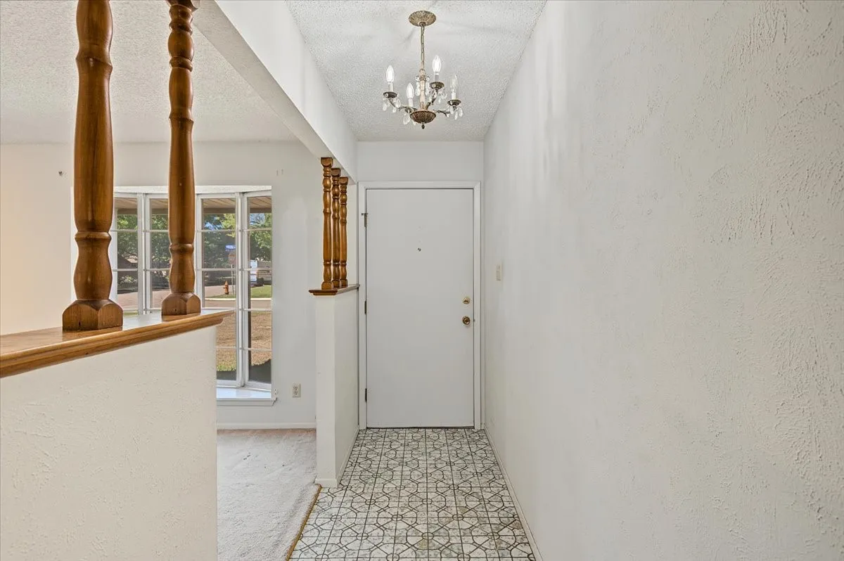 Entryway featuring patterned floor tile, white door, and a chandelier