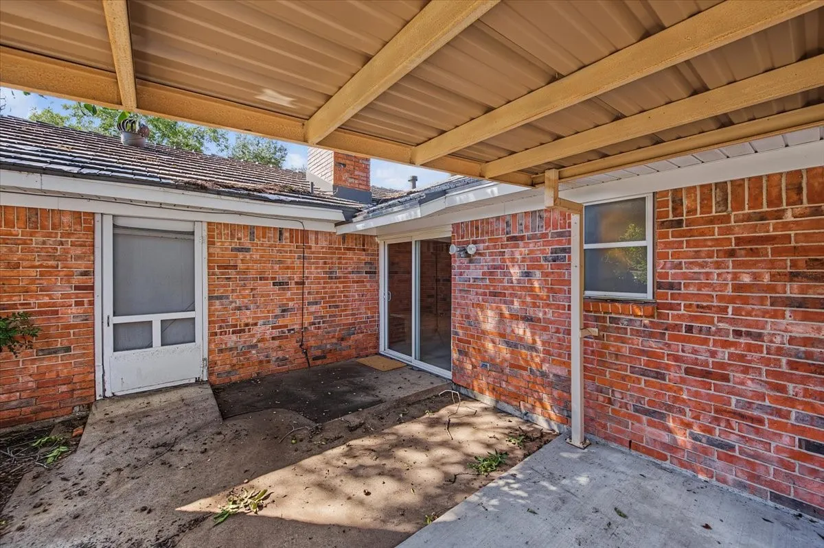 Covered patio with a corrugated metal roof, brick exterior, and a sliding glass door